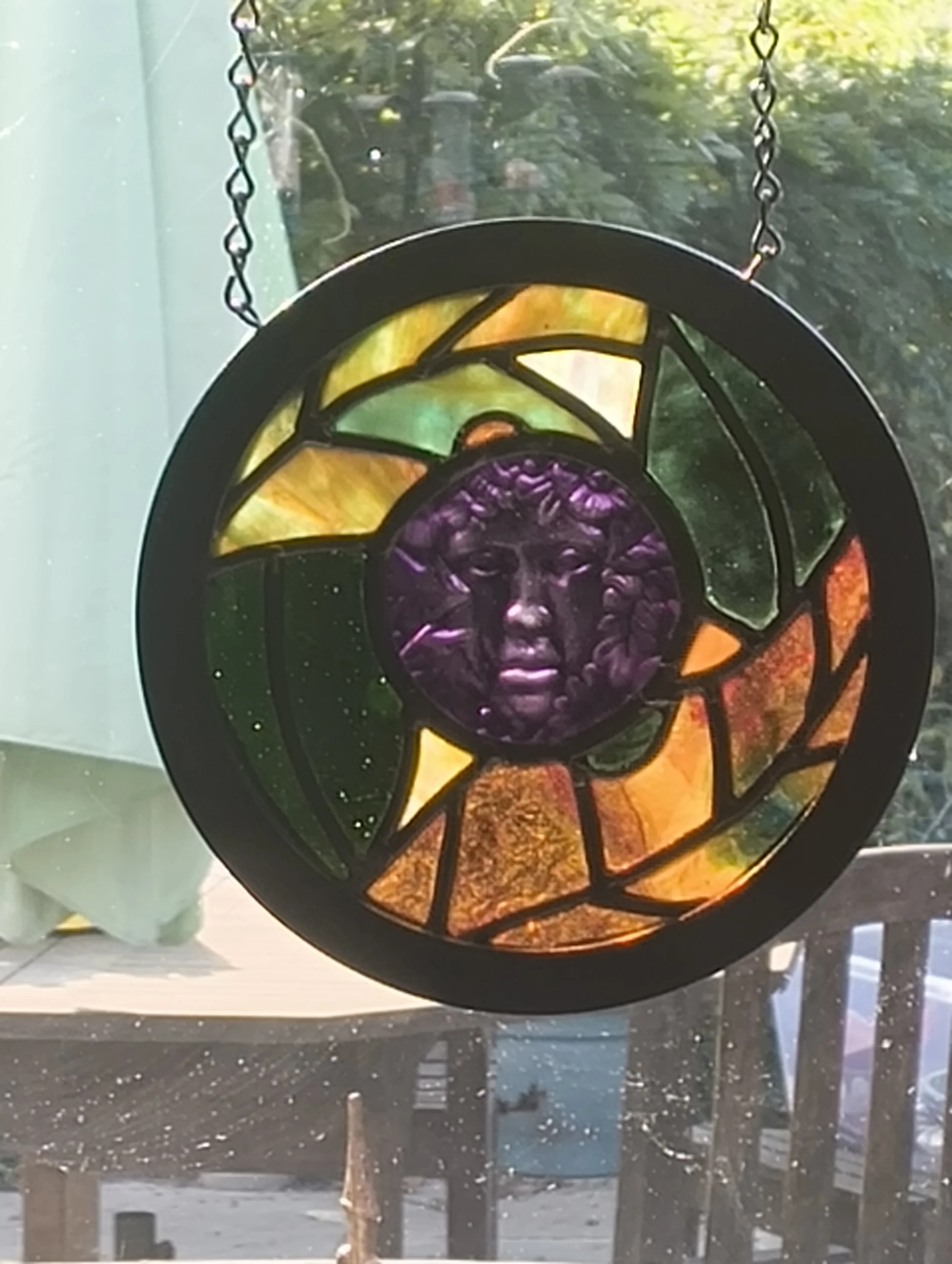 Violet Muse stained glass wall hanging with a violet face, backlit by the sun