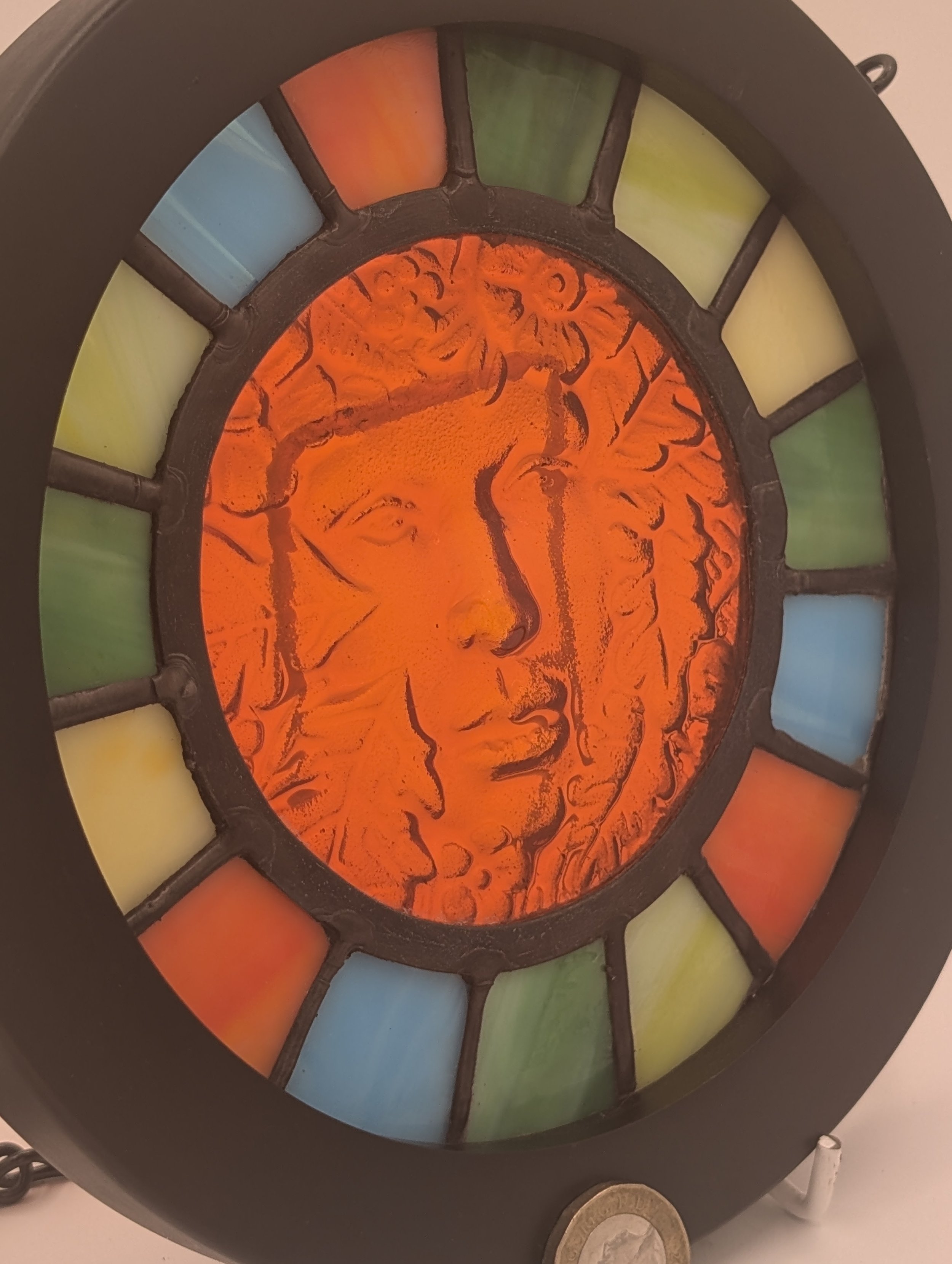 Close-up of Amber Muse's textured amber glass face with leafy hair, framed by green, blue and orange panes