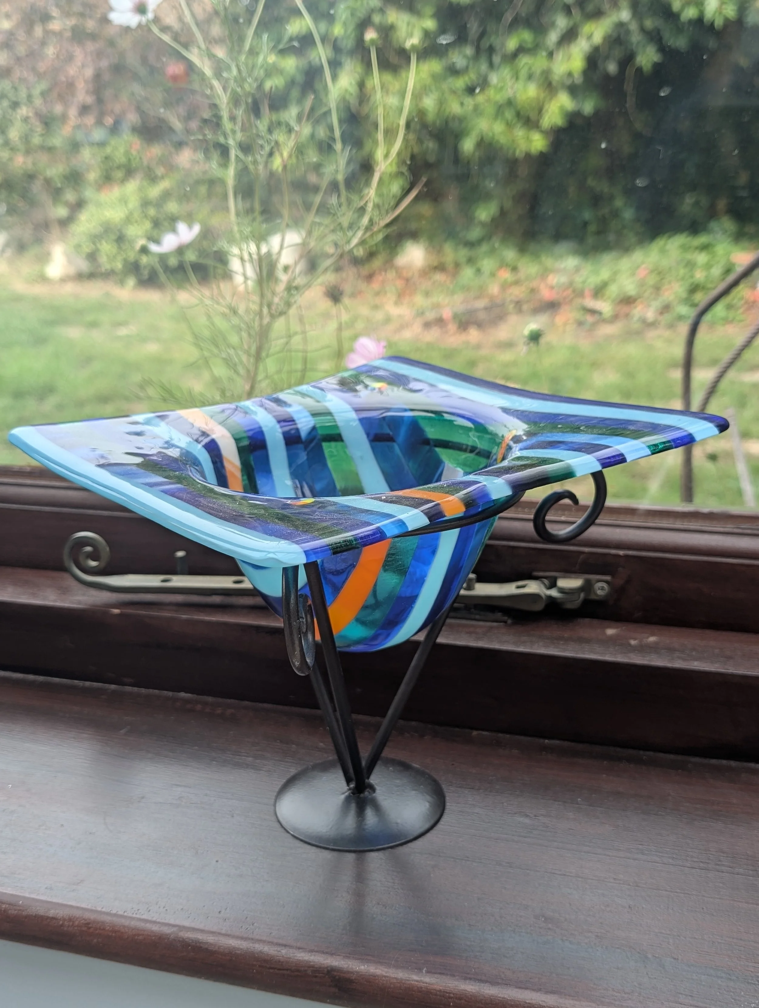 Ocean Ribbon fused glass vessel glowing in navy, cobalt, turquoise and teal stripes in a sunny window