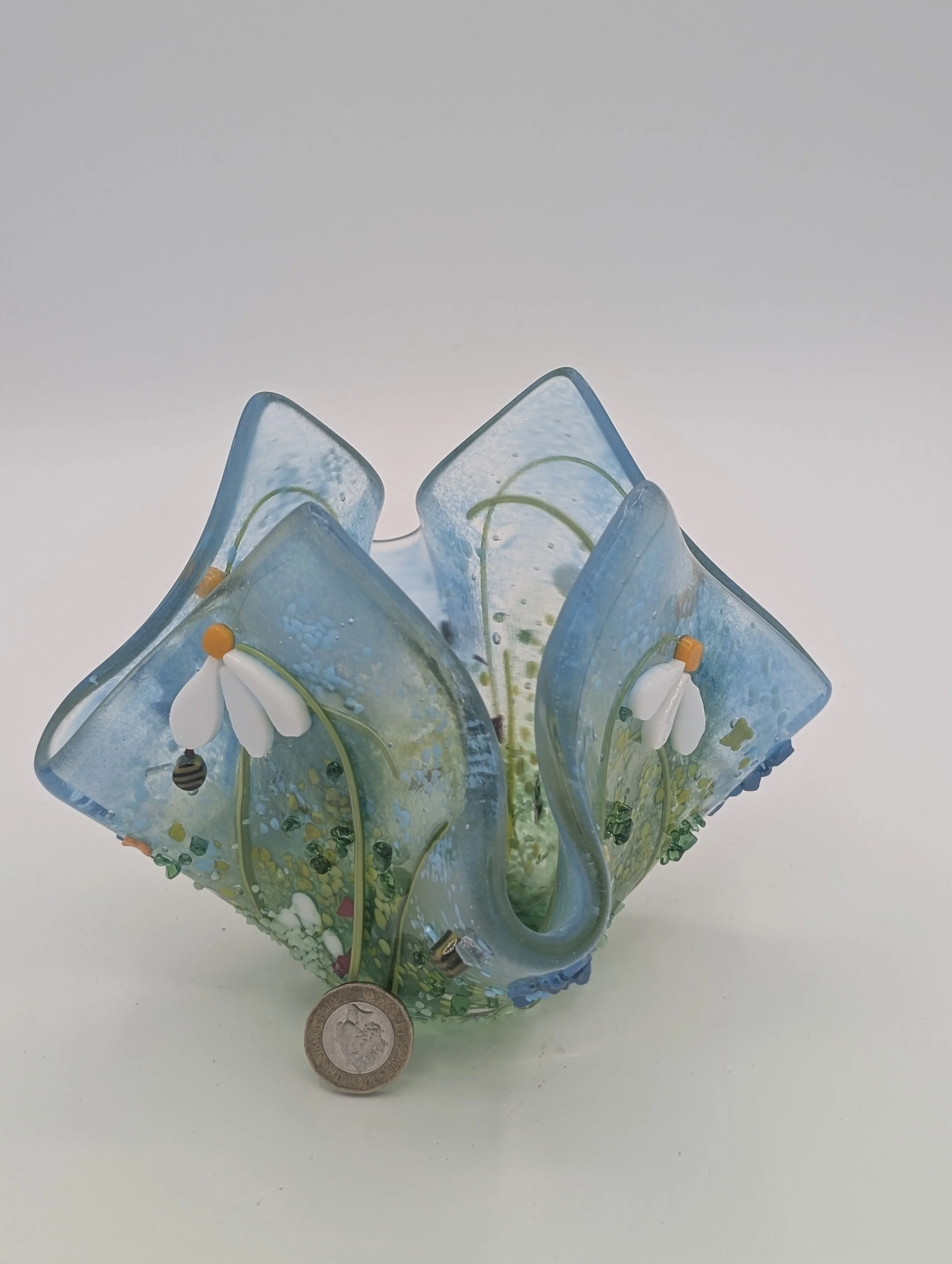 Meadow Dew fused glass vessel front view: white daisies with orange centres and a tiny bee, £1 coin beside