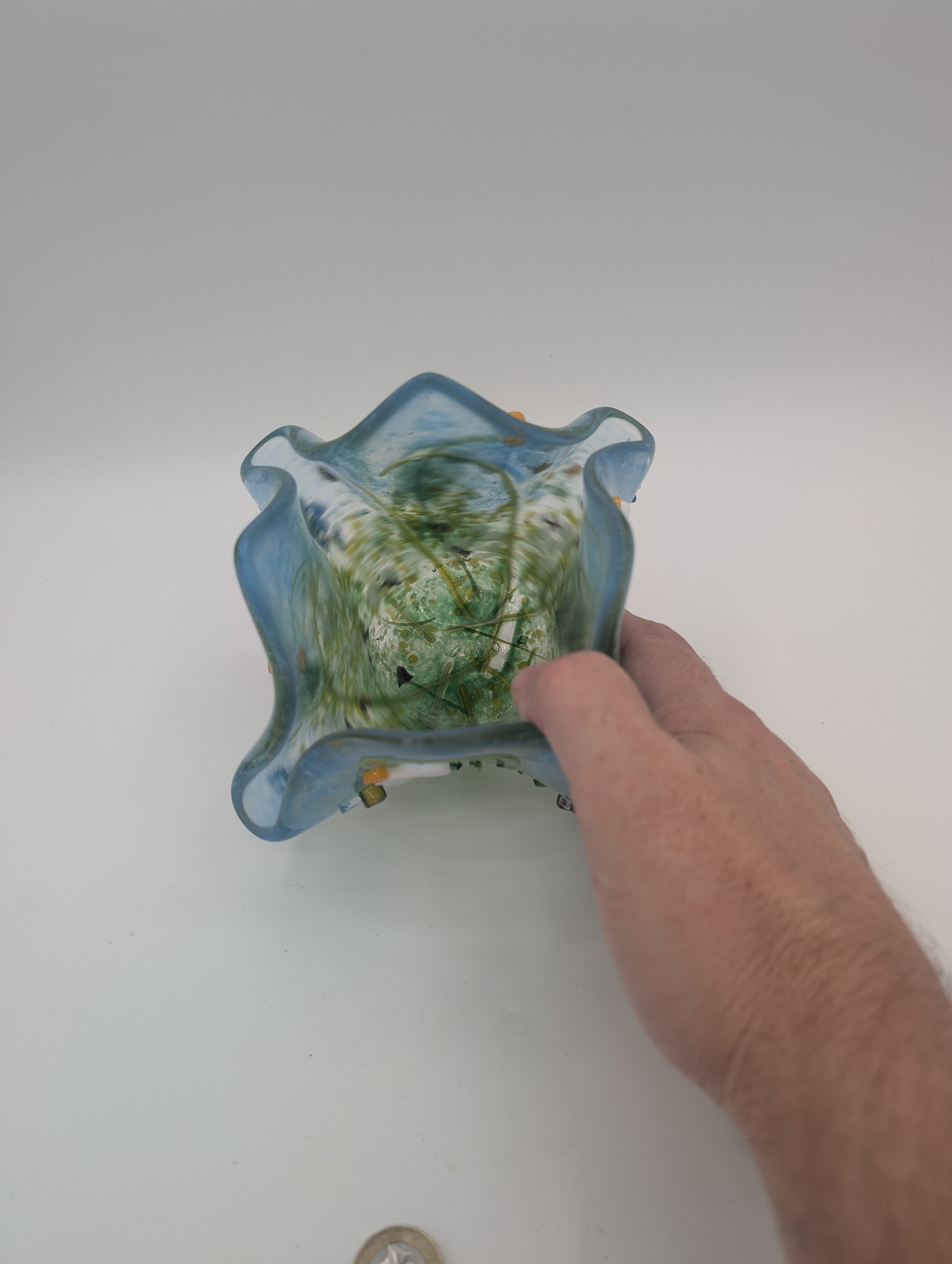 Hand holding Meadow Dew fused glass vessel seen from above, showing its green speckled interior and wavy rim
