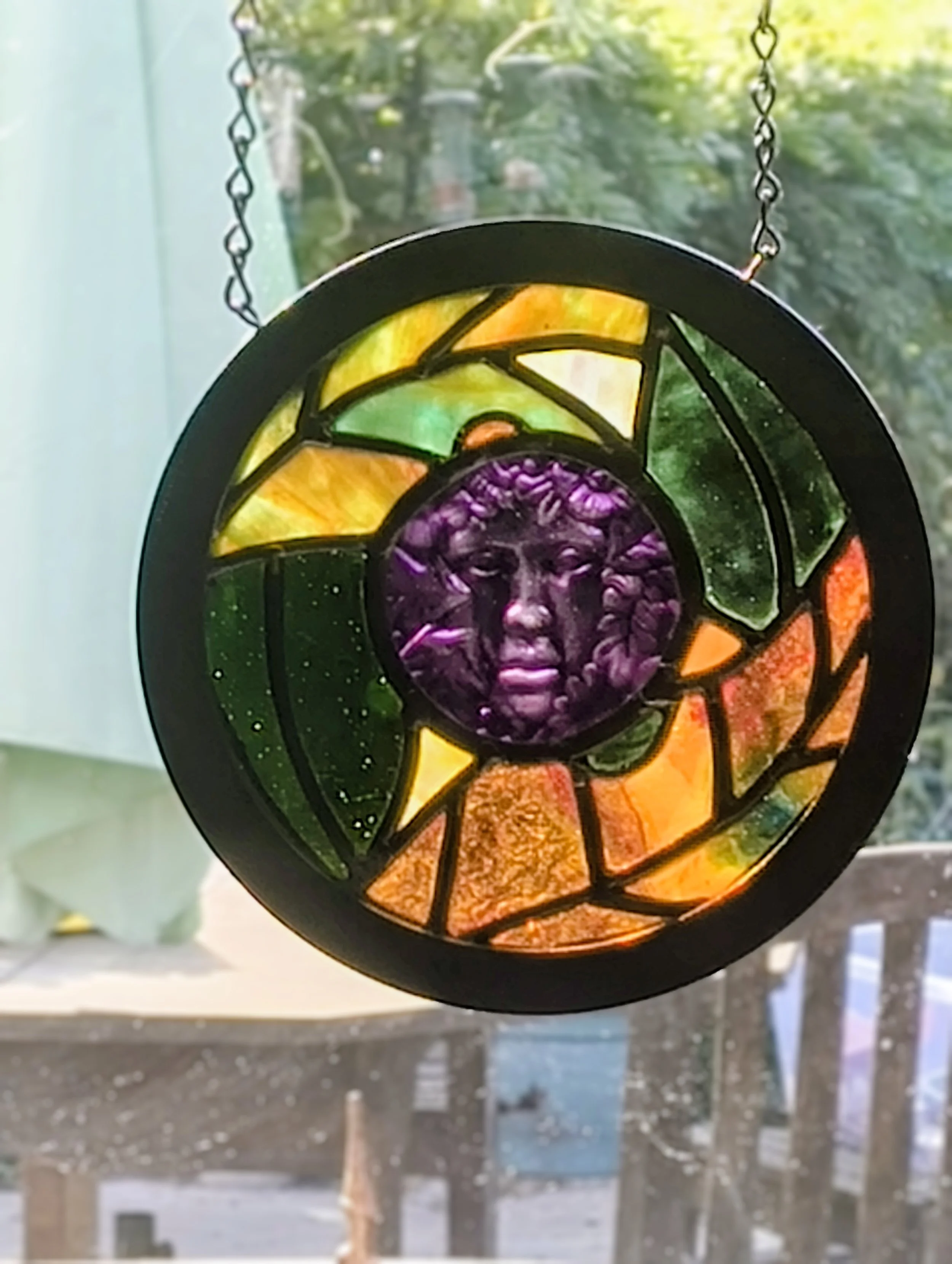 Violet Muse stained glass wall hanging with a violet face, backlit by the sun