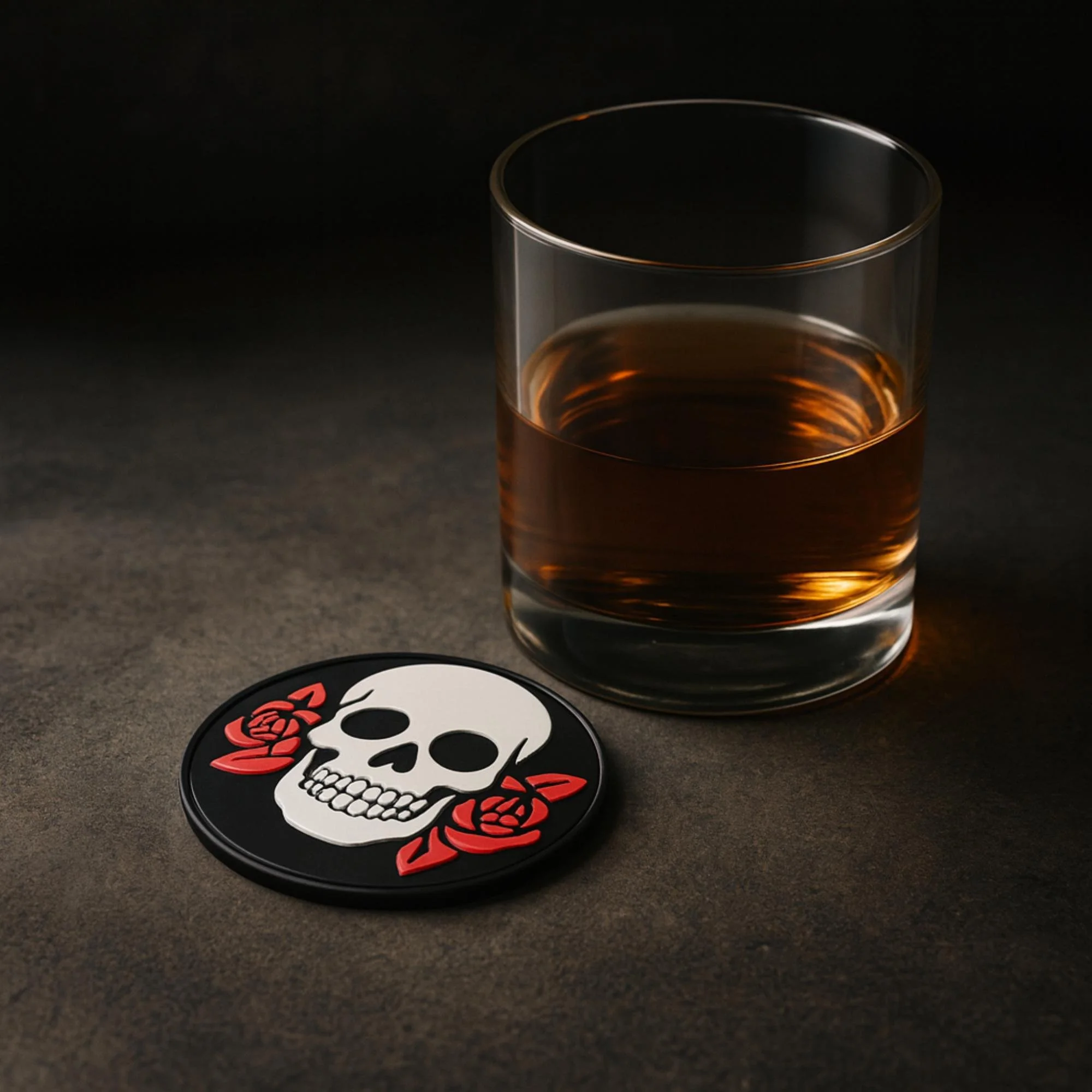 Black 3D-printed coaster featuring a white skull with red roses, styled next to a glass of dark-colored drink on a dark textured tabletop