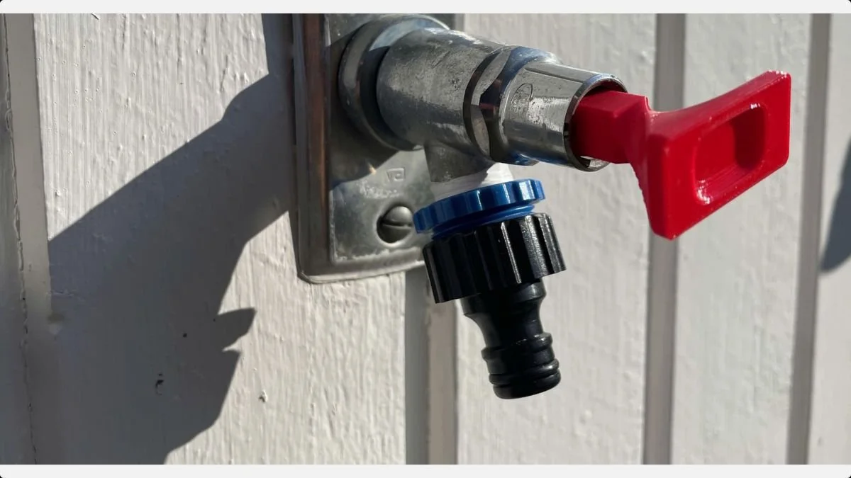 Red 3D-printed sillcock key inserted into an outdoor tap above a hose connector.