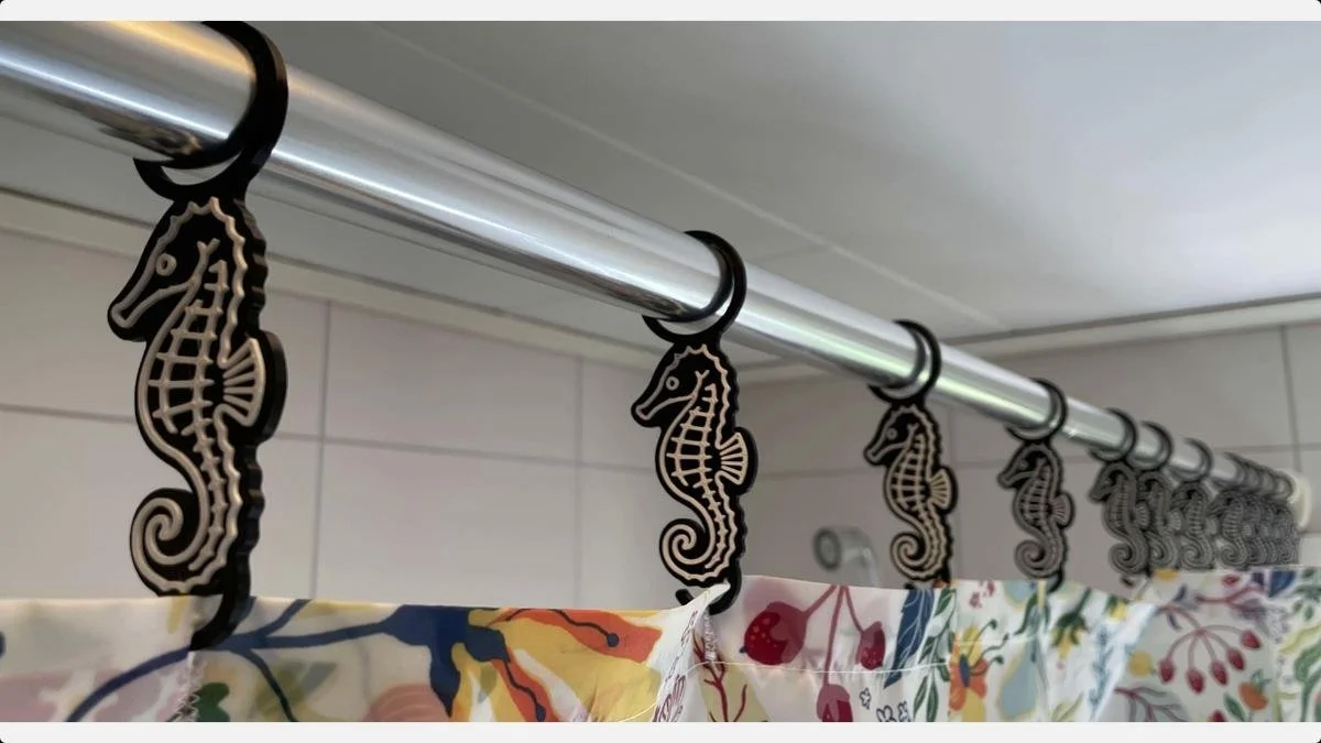 Printed seahorse hangers suspended from a shower curtain rod above a patterned curtain.