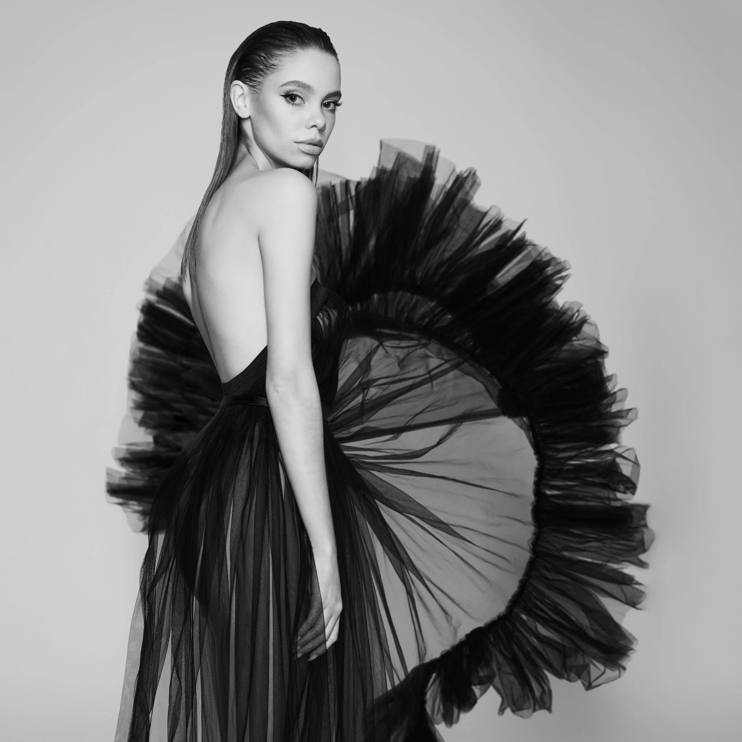 Black and white photo of a woman in an elegant, backless gown with a dramatic tulle skirt.