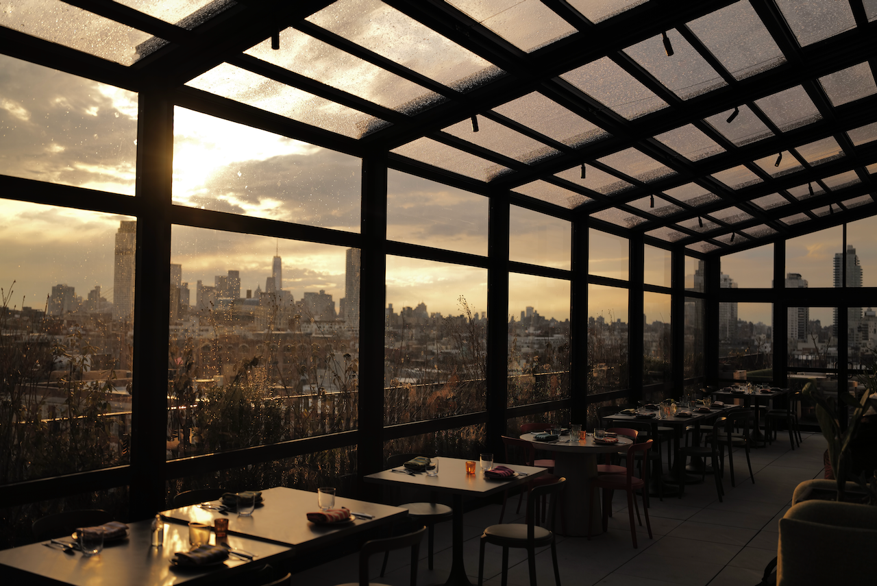 Indoor restaurant with large glass windows showcasing a city skyline at sunset