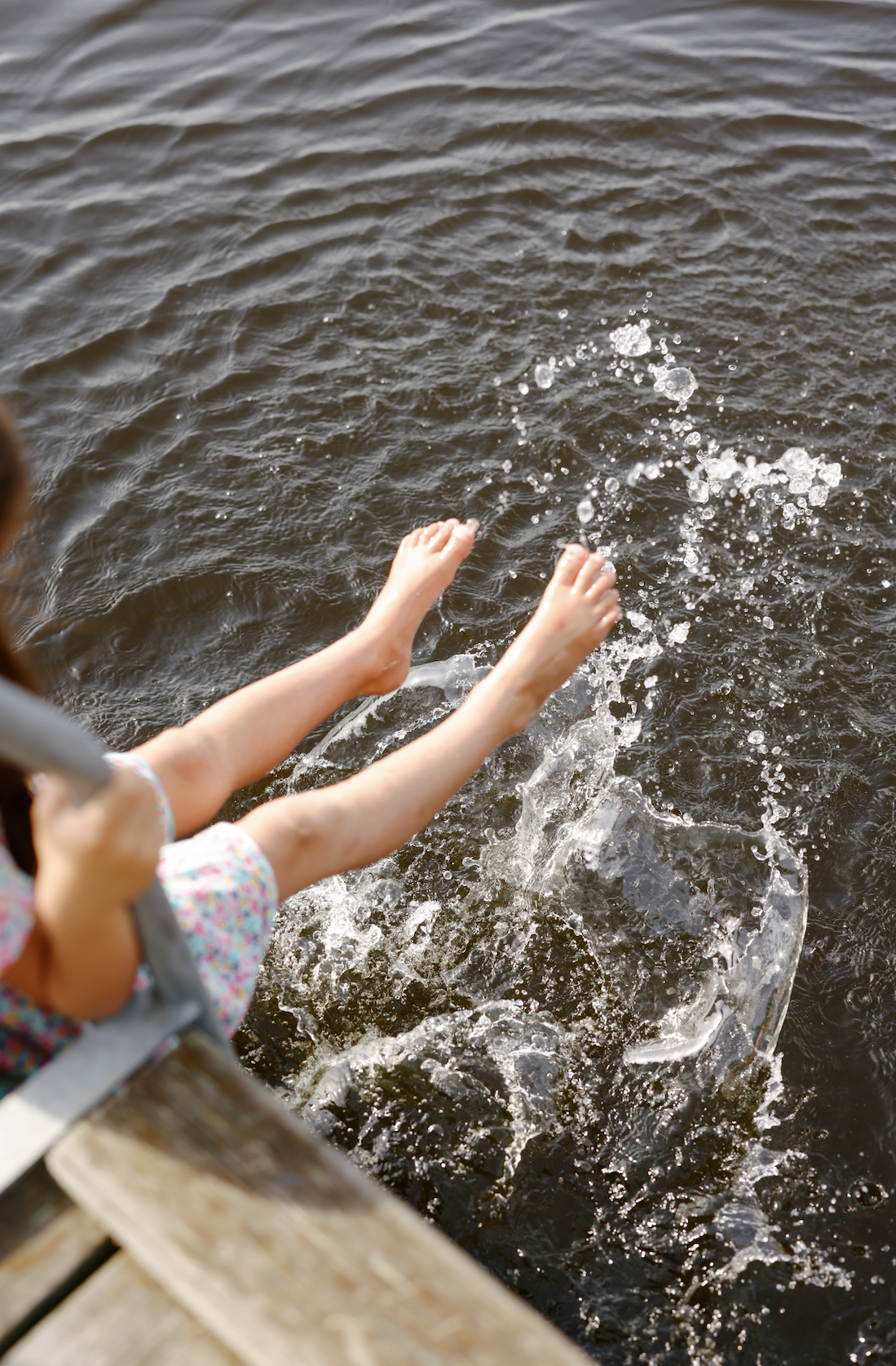 Child splashing water into a body of water, seen from above, near a wooden dock.
