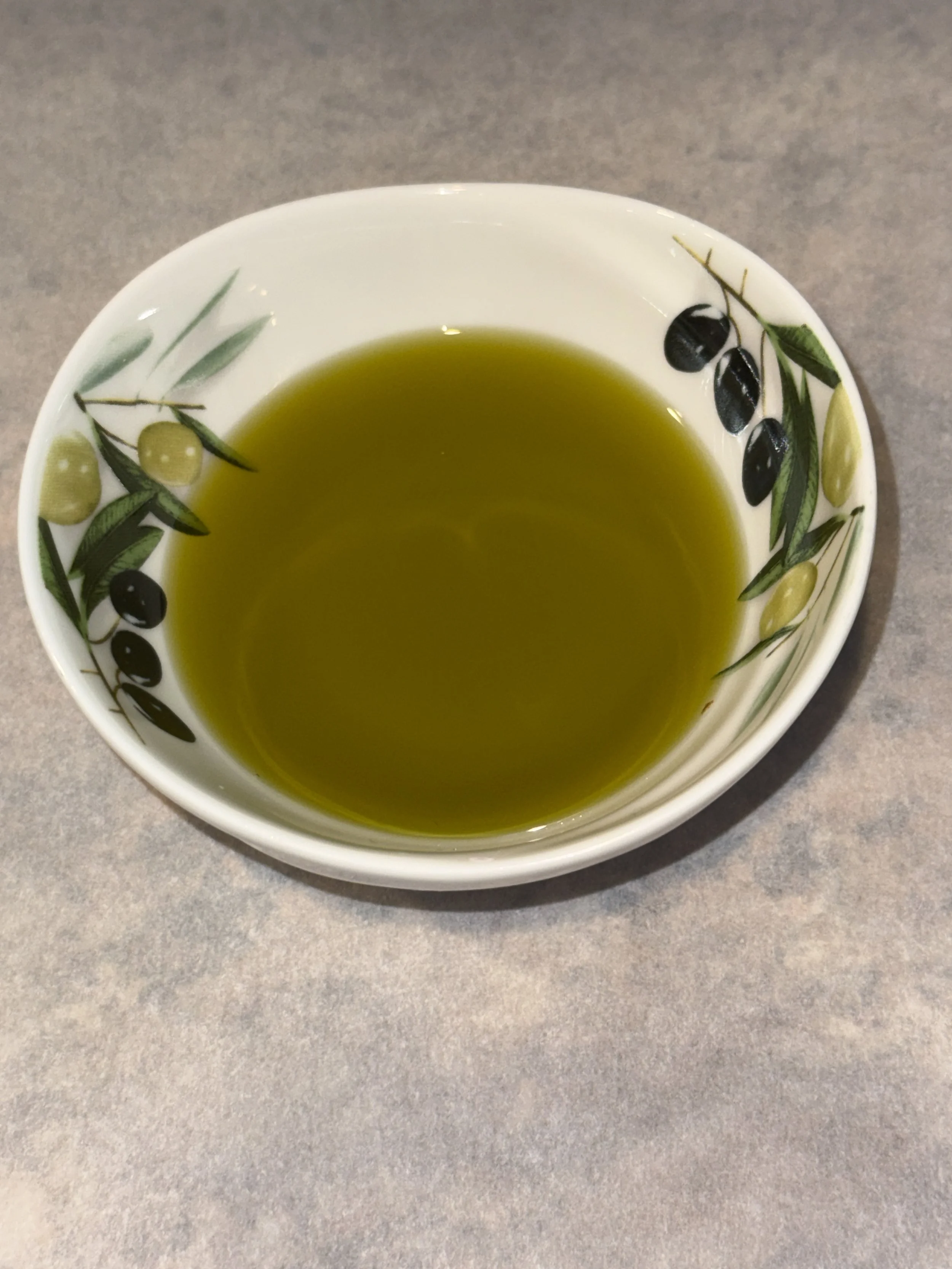 A bowl filled with green tea on a gray surface, with a white exterior decorated with olive branches and olives.
