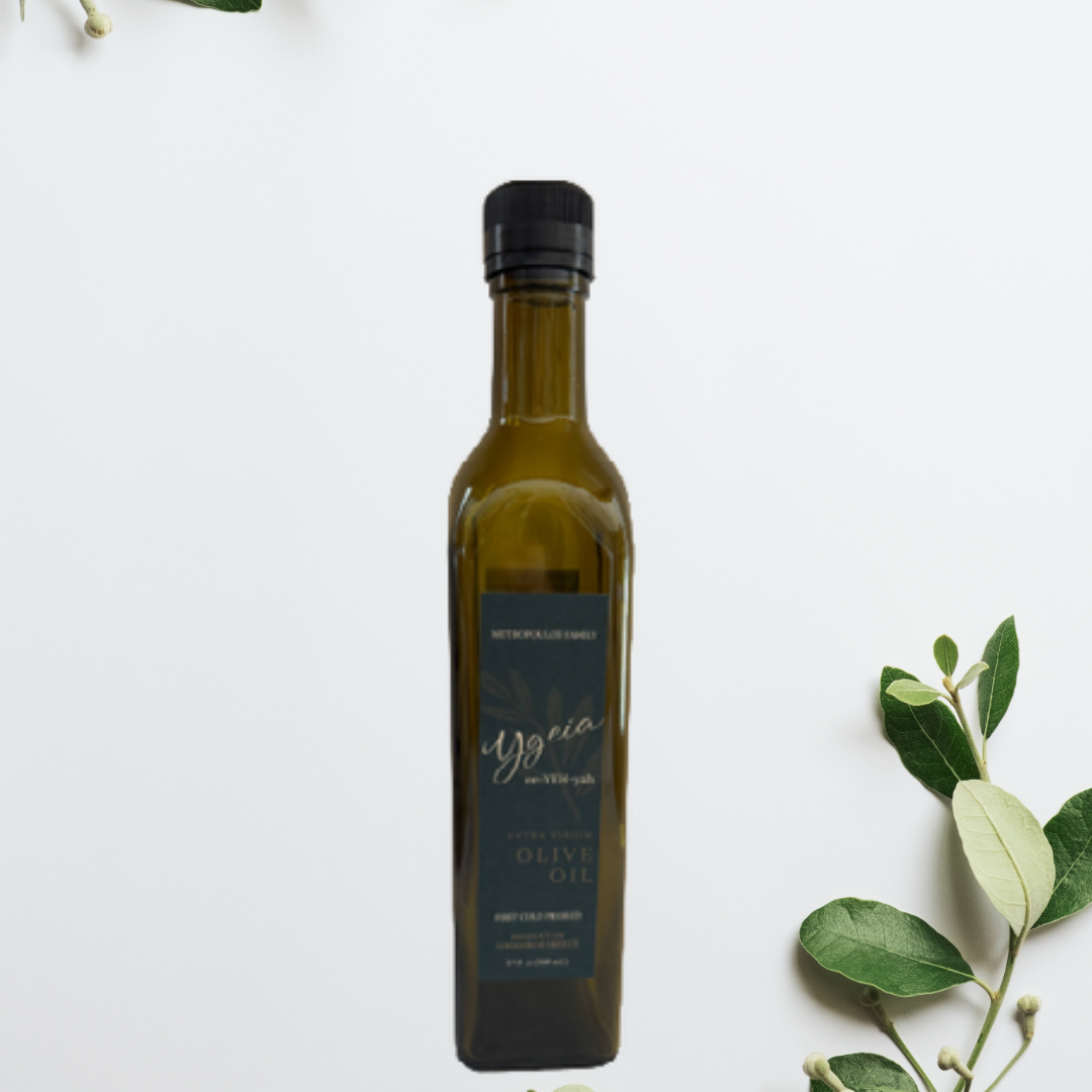 A bottle of extra virgin olive oil with a black cap and a blue label, placed on a white surface with some green leaves on the right side.
