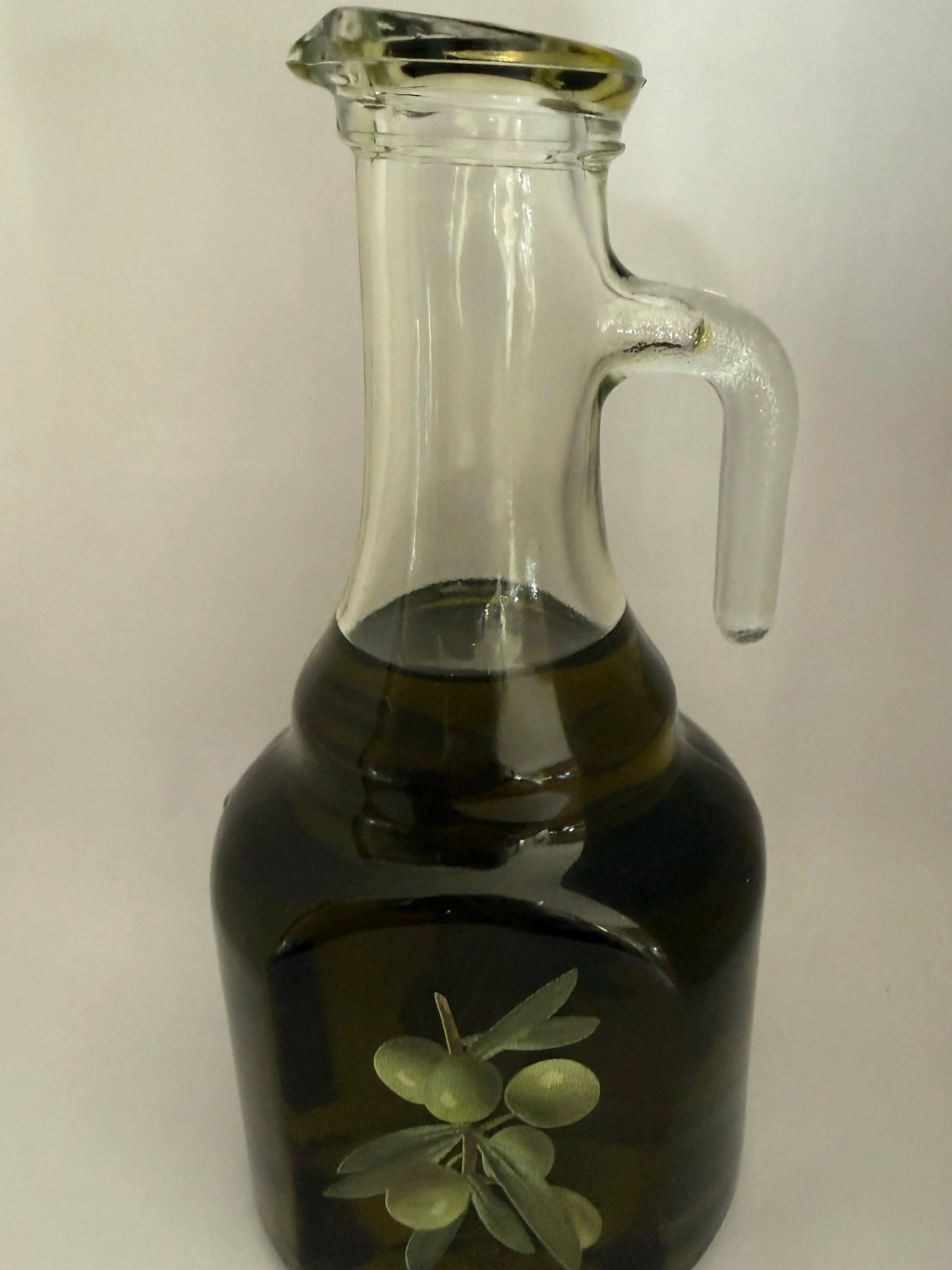 A glass bottle filled with dark olive oil, featuring a label with an illustration of an olive branch with green olives and leaves.