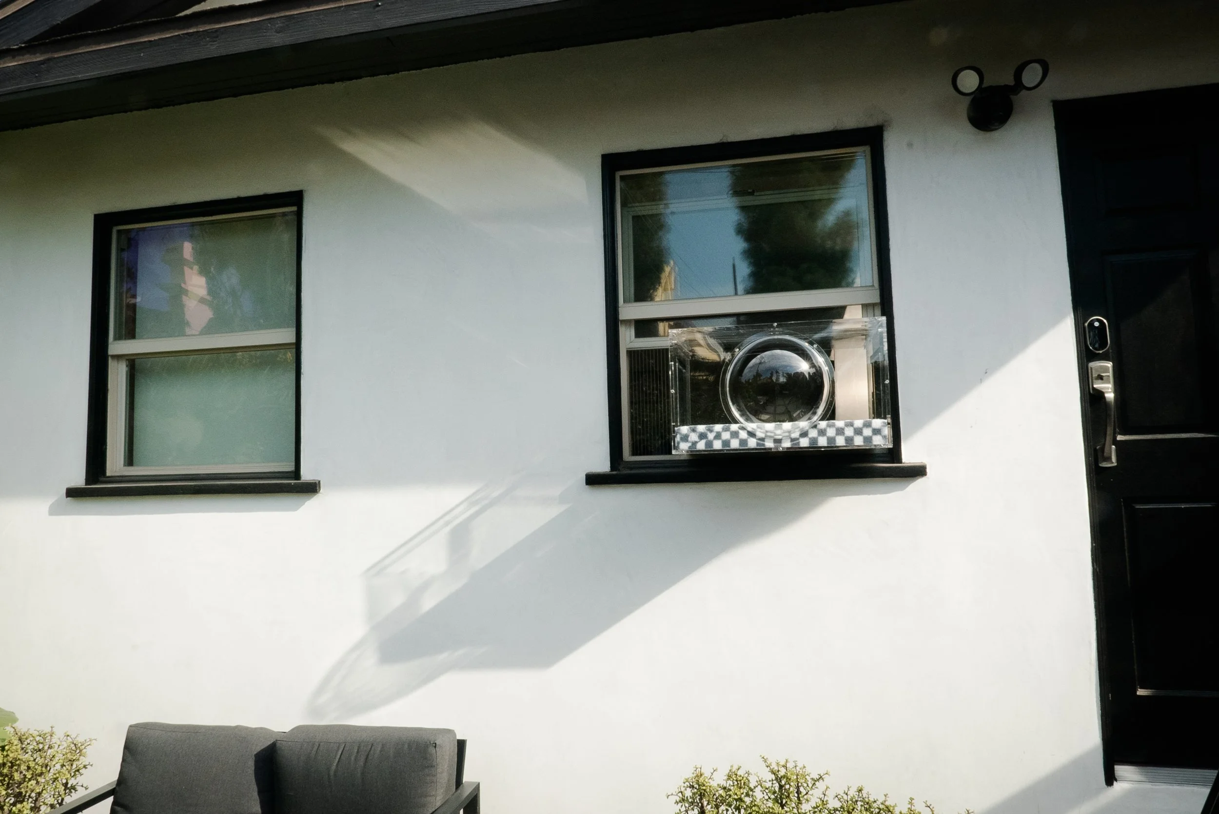Exterior of a white house with a black door, two windows, and a pet door Window Catio. Catio.