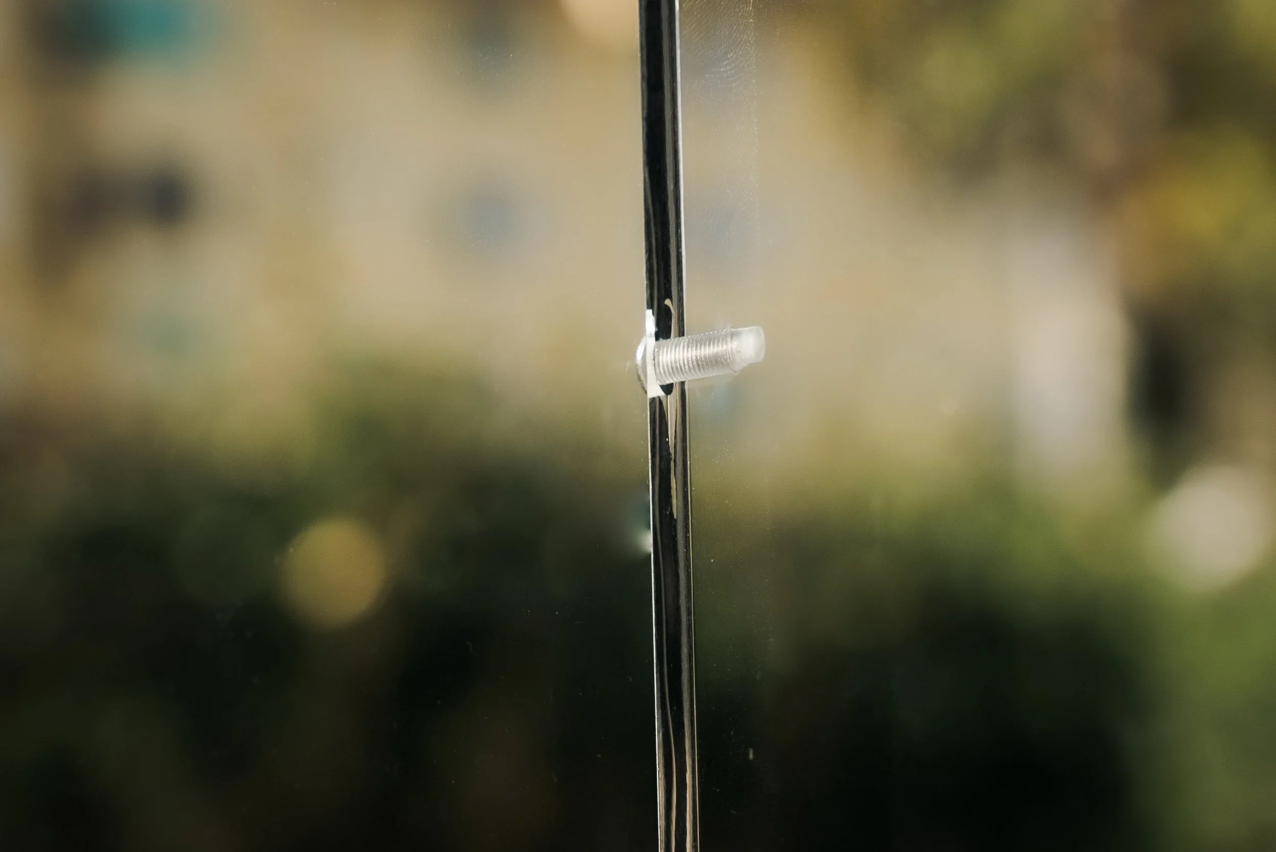 Close-up of a transparent plastic rivet on a glass surface with a blurred outdoor background.