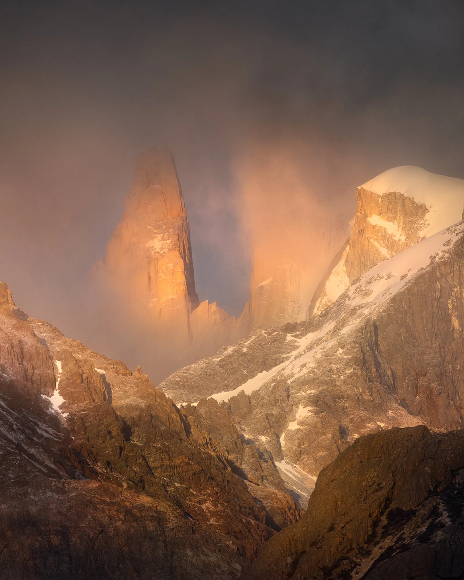 The towering granite spire, Aguja Rafael Juárez, stands illuminated in the soft light of dawn, surrounded by a backdrop of scattered clouds. Its rugged contours and sharp silhouette against the sky highlight the awe-inspiring beauty of Patagonia’s mo