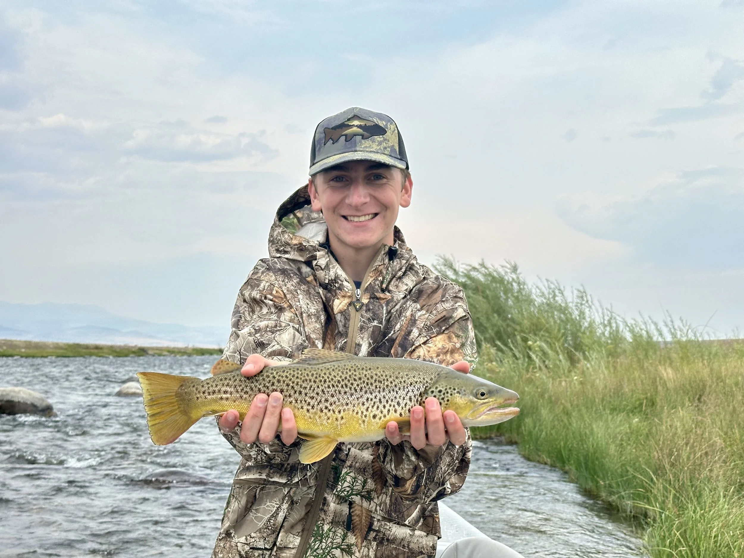 Young man holding a nice brown trout caught on a streamer in the Madison River on a guided fly fishing trip