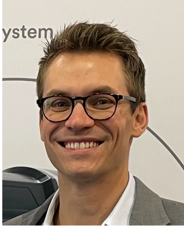 Portrait of a smiling young man wearing glasses, in front of a white background with partial text and a diagram.