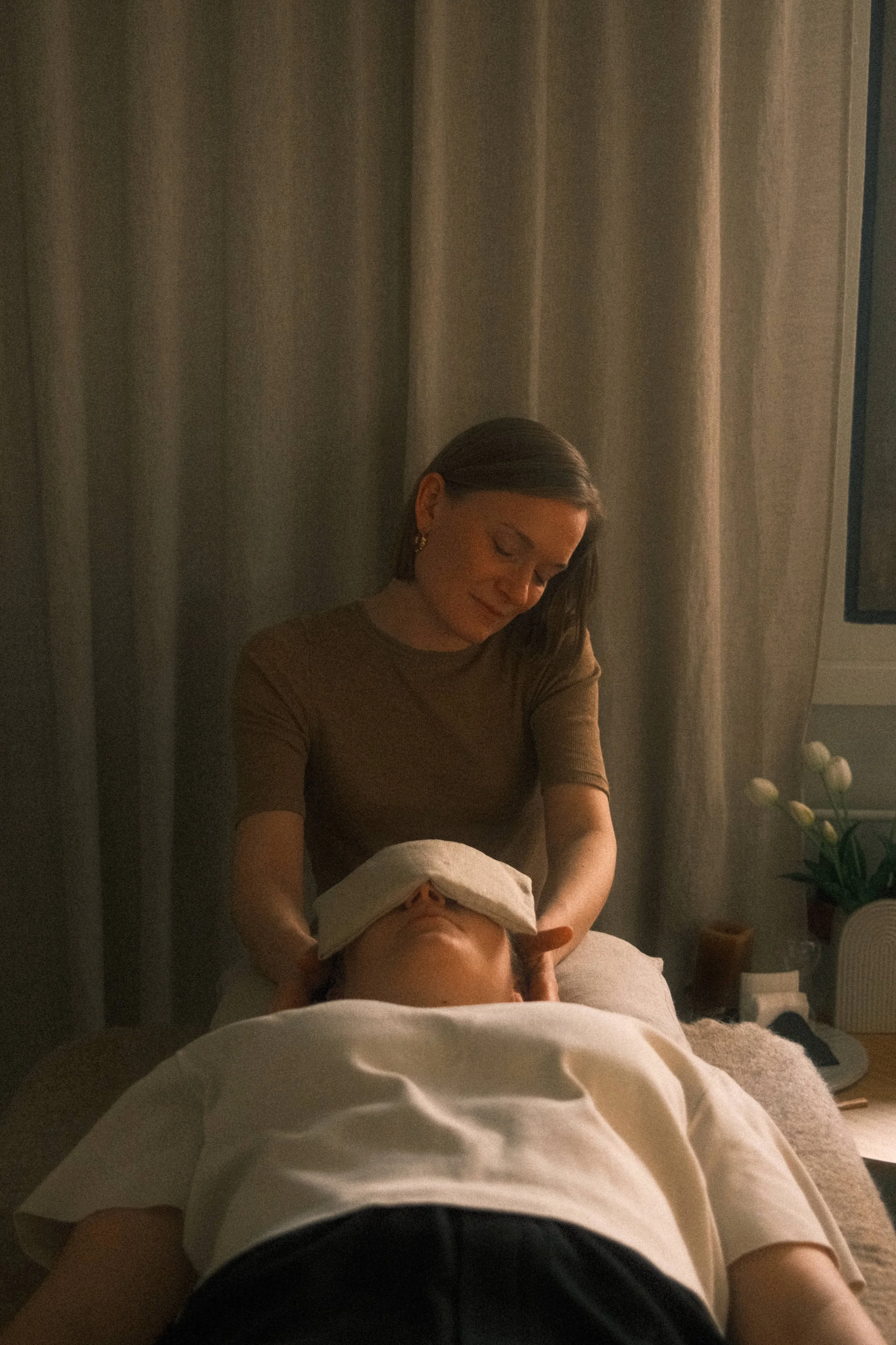 En kvinde får en massage fra en anden person i et hjemmemiljø. Der er planter og en skærm synlig i baggrunden.