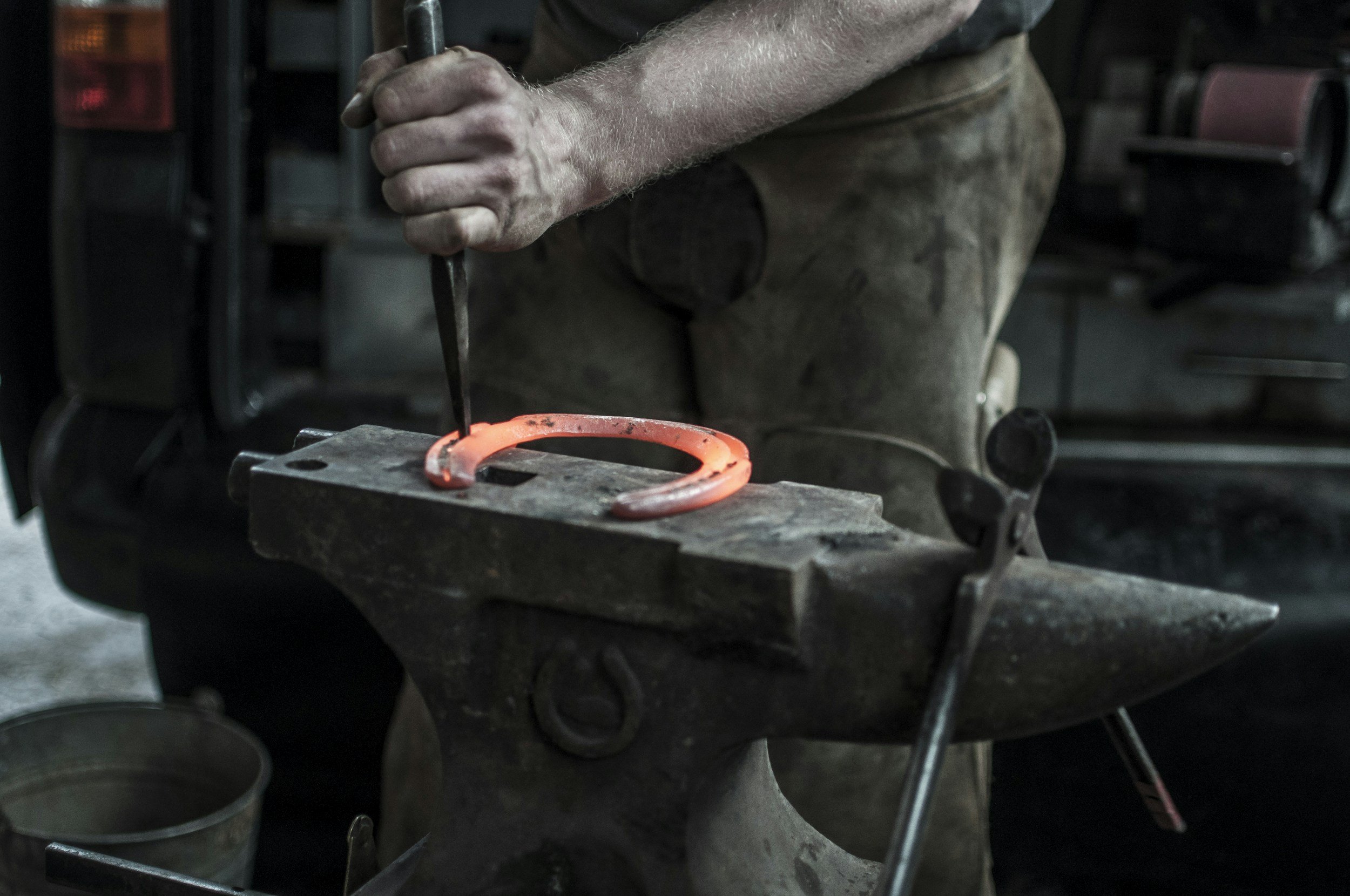 Blacksmith crafting a hot iron horseshoe on an anvil with a chisel and hammer.