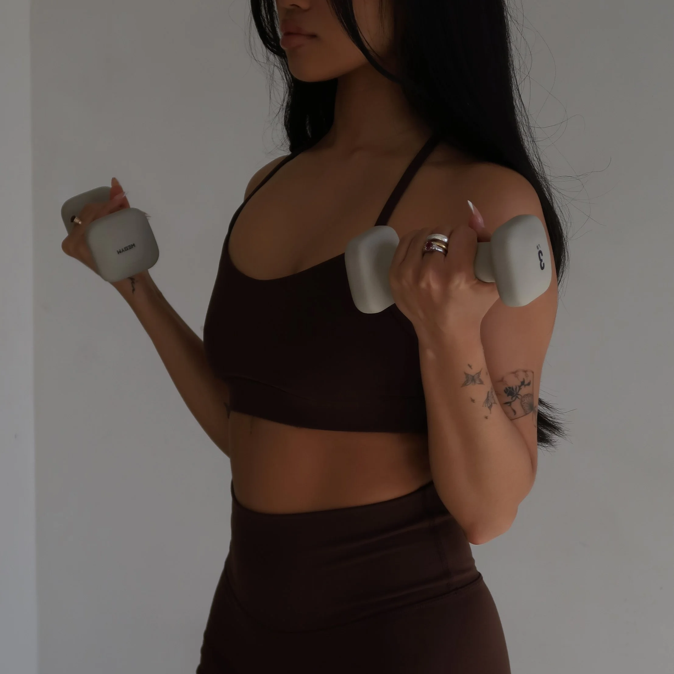 Fit woman bicep curling dumbells in a dark brown activewear set