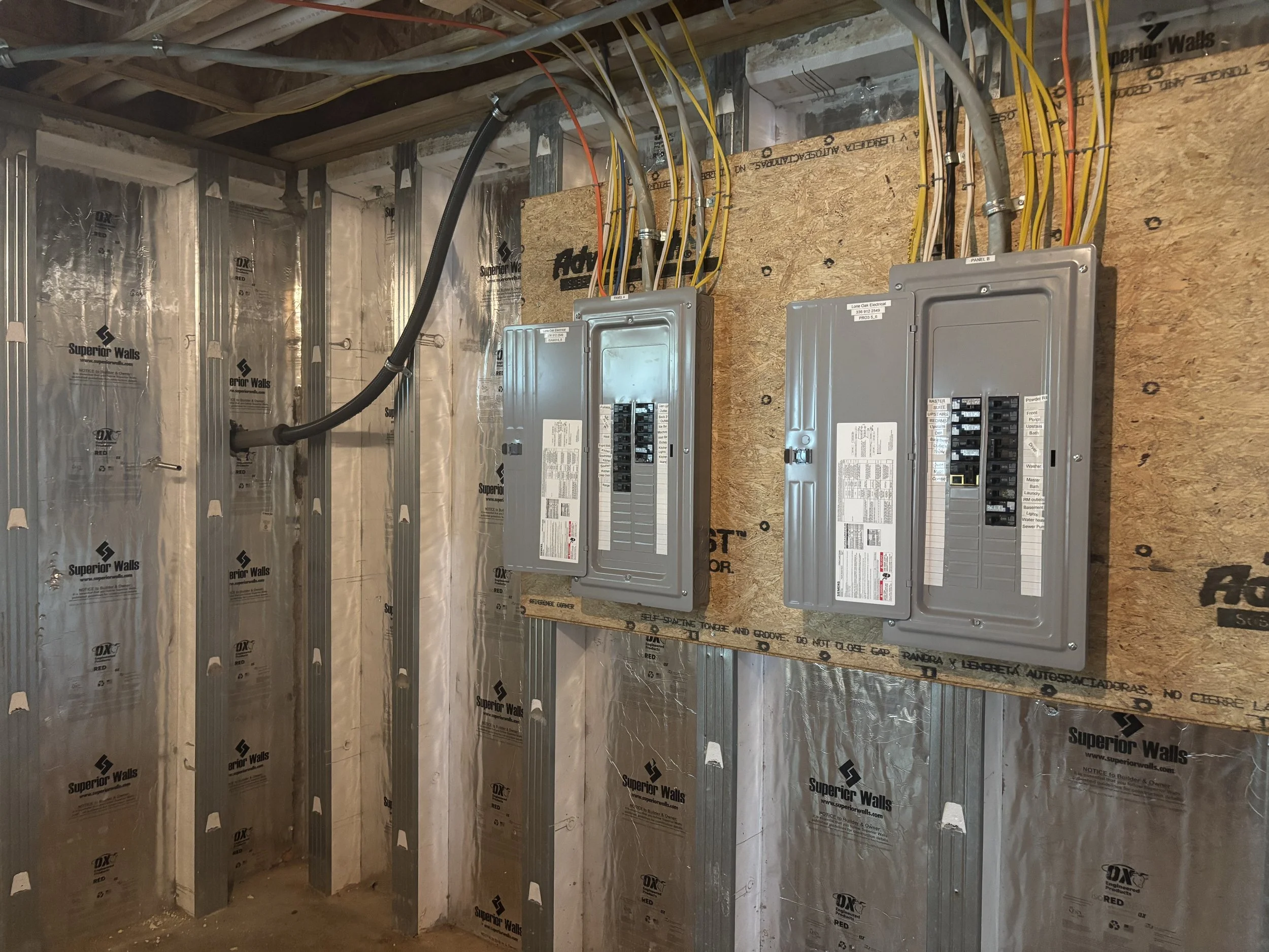 Electrical panel boxes and wiring installed inside a construction room with insulation and drywall framework.
