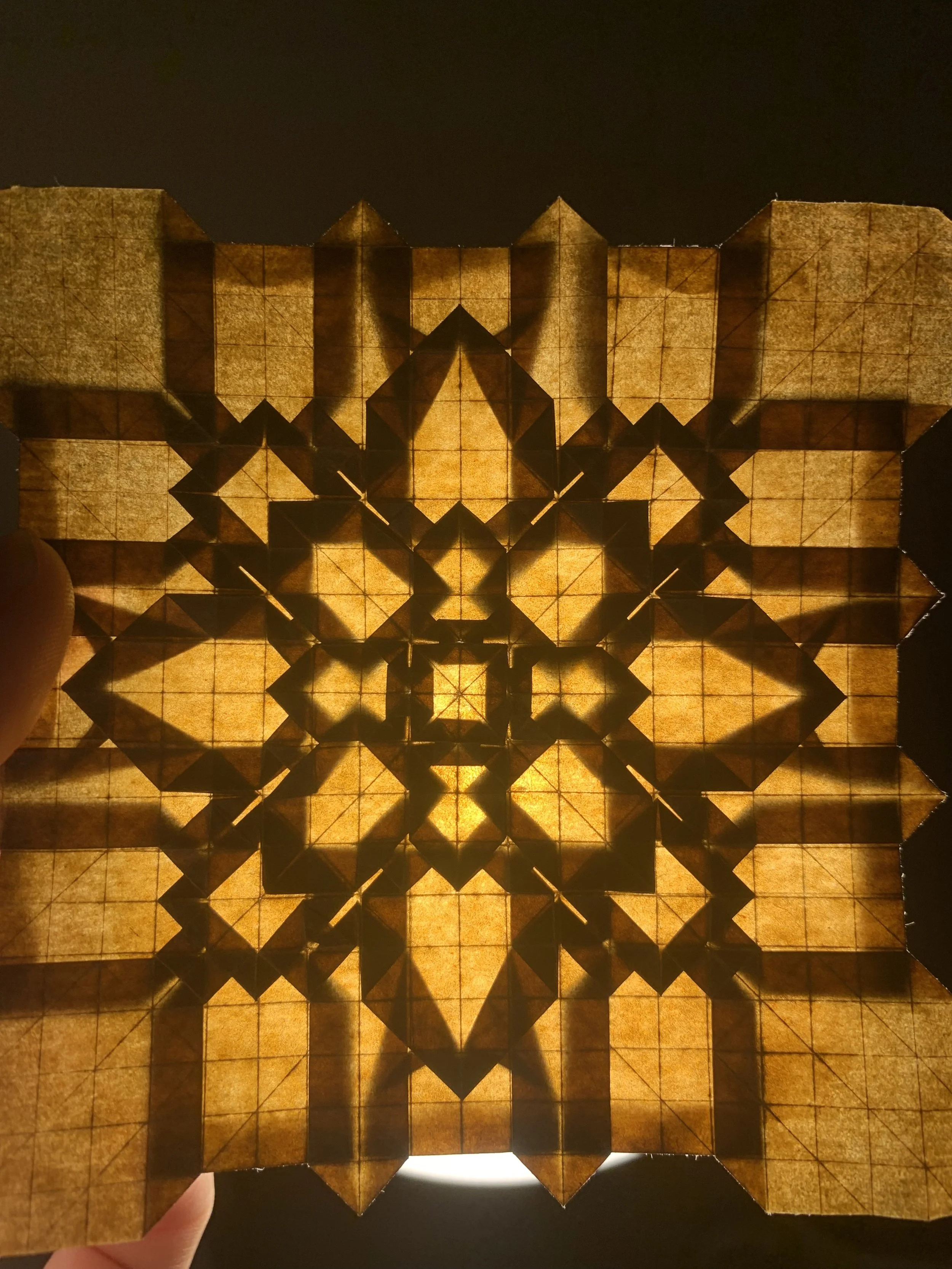 A person holding a gold-colored 3D cube puzzle with intricate geometrical design and shadows it casts.
