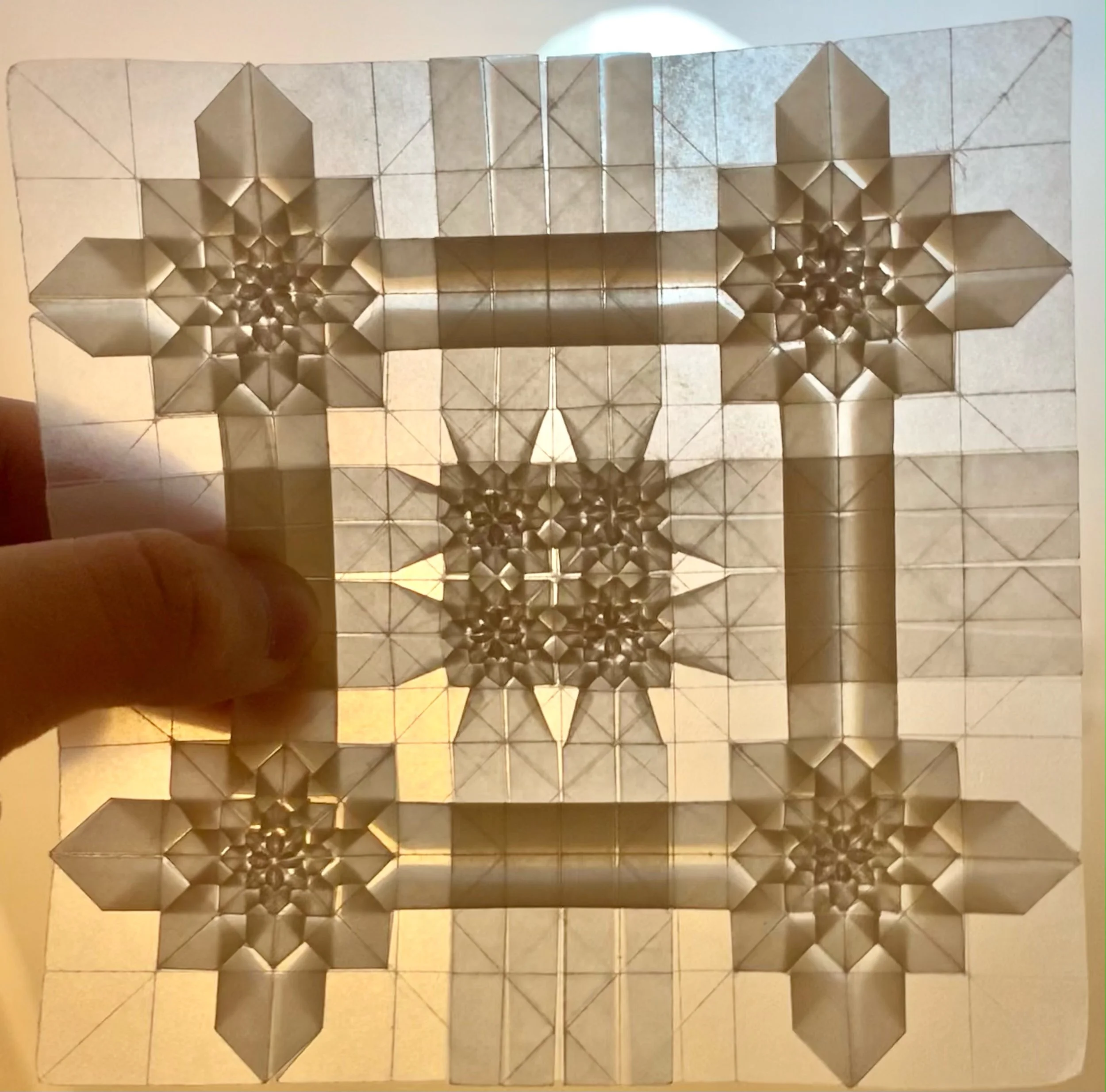 origami tessellation of a group of metallic, reflective building blocks assembled into a three-dimensional geometric structure with three stars or flower shapes on each side.