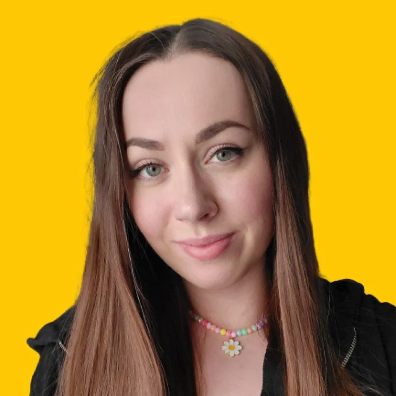 A young woman with long brown hair, wearing a black top and colorful bead necklace, smiling slightly against a bright yellow background.