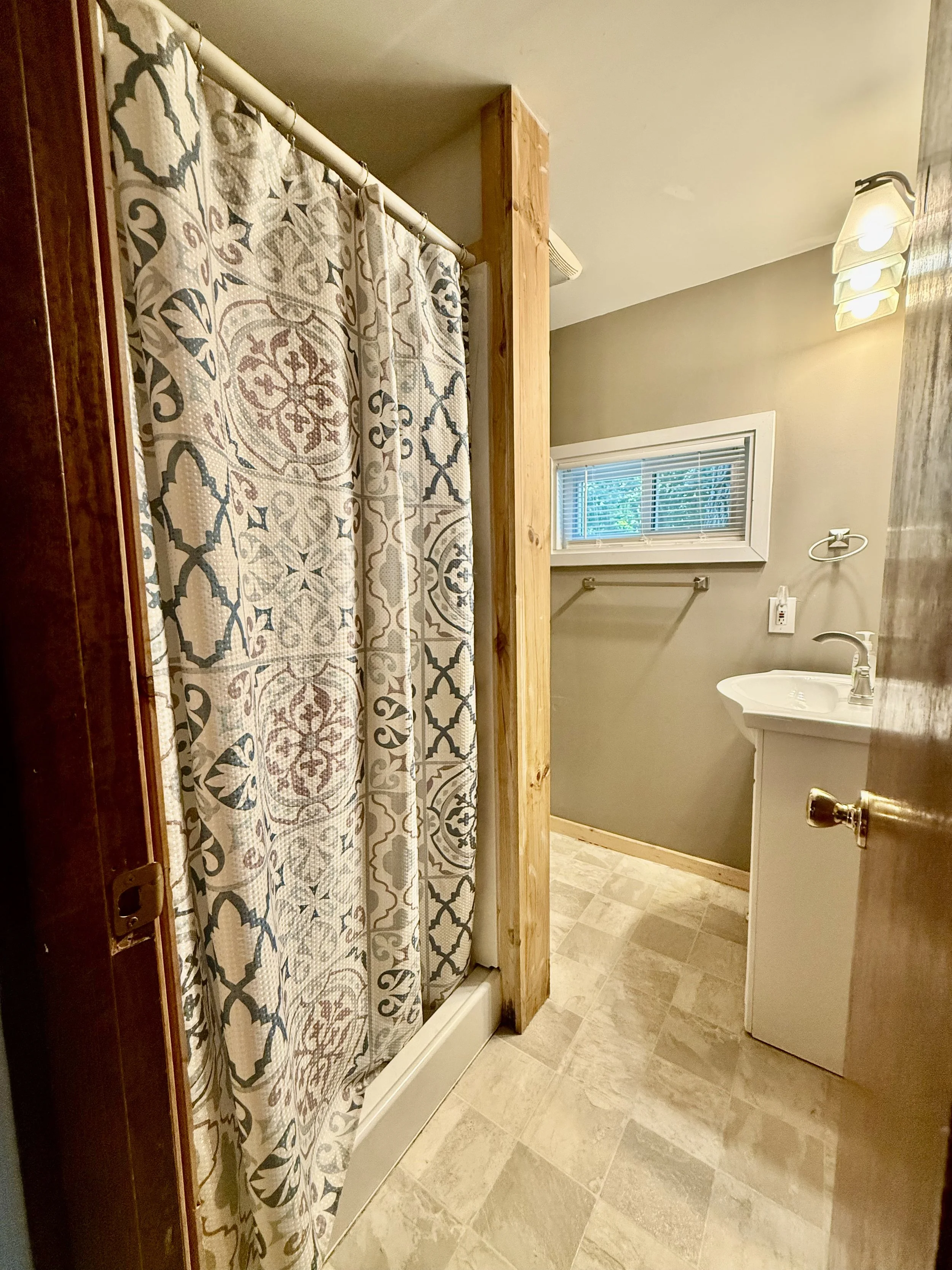 Bathroom with a shower curtain, small window, white sink, and beige tiled floor.