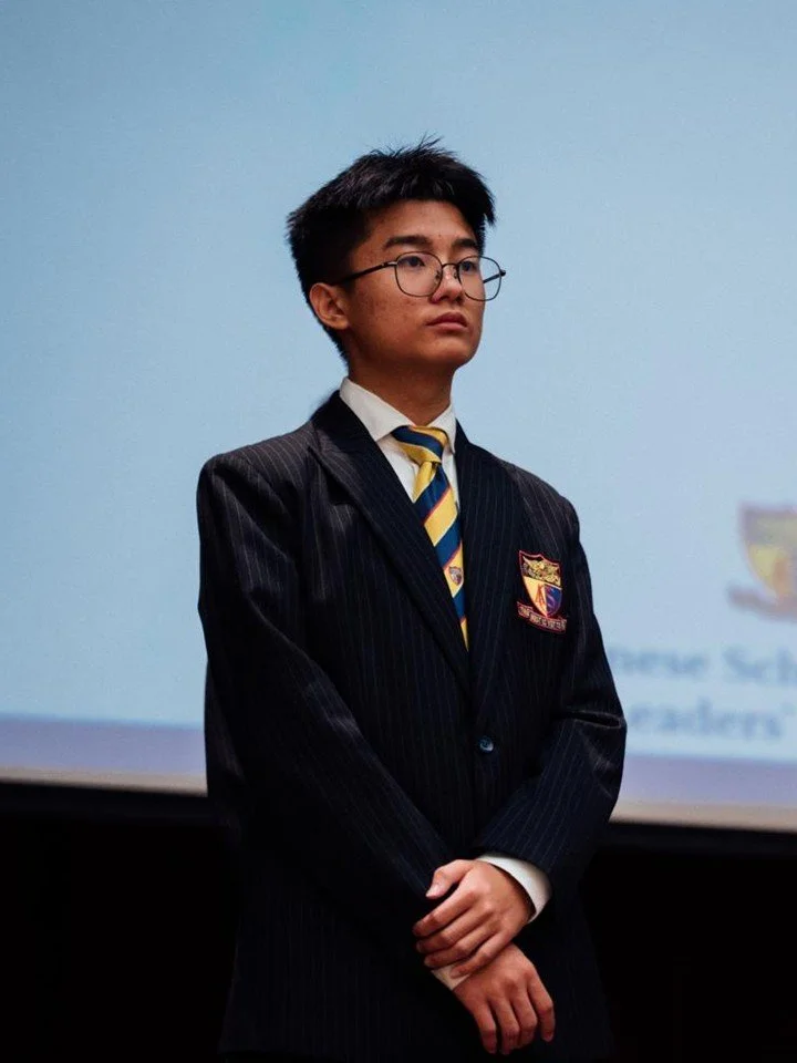 Jerome Ong in school uniform standing on the stage in a darkened auditorium.