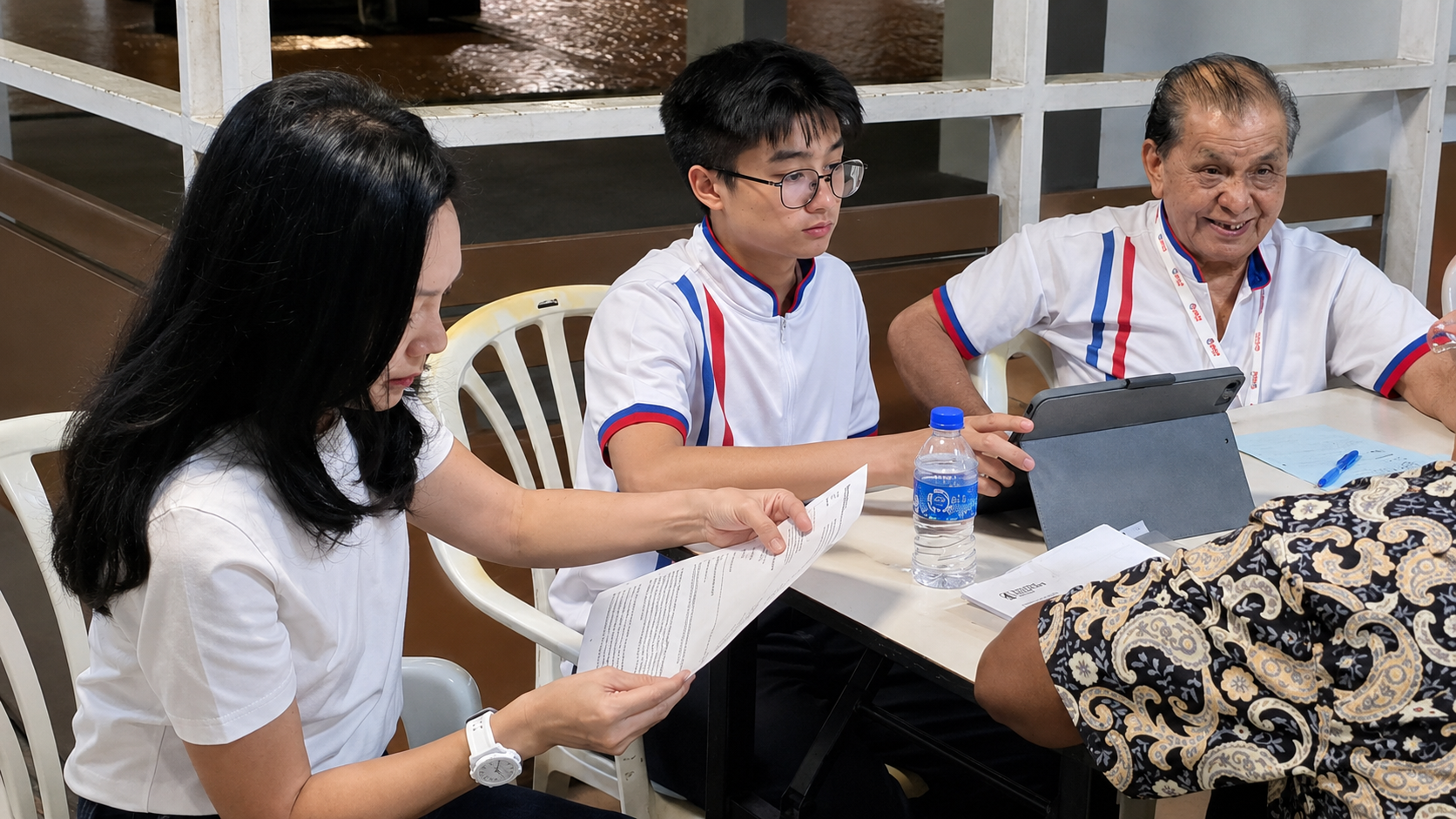 Jerome Ong and the Member of Parliament seated with a resident at a Meet-the-People Session, reading documents on a tablet.
