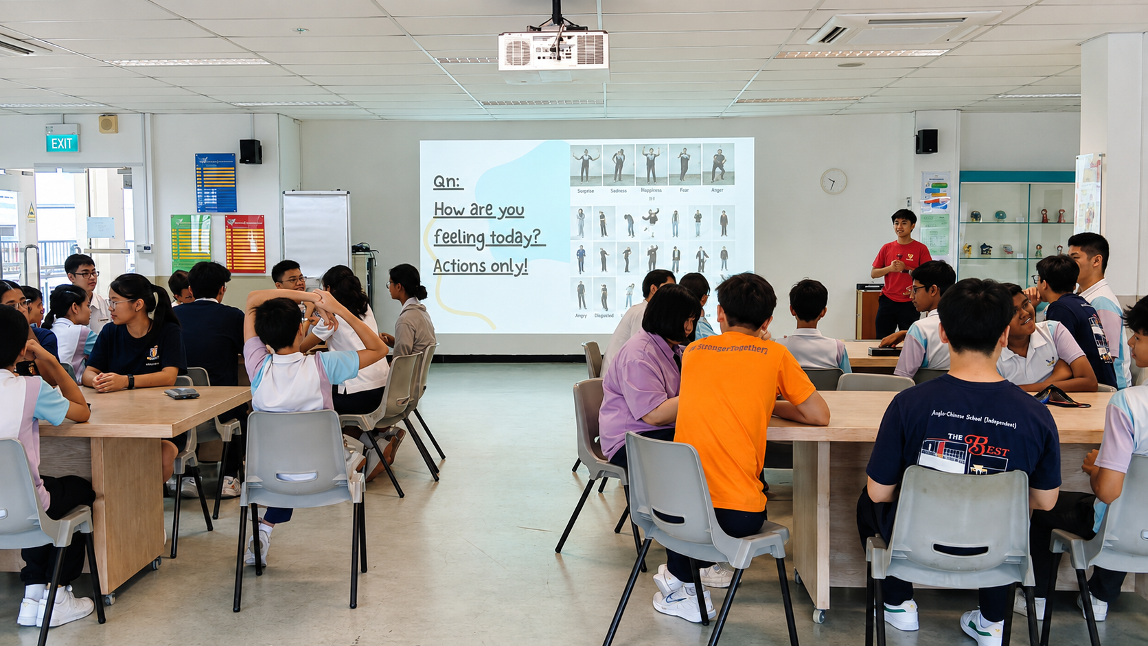 Students at tables in a Project Flare workshop, facing a slide asking them to answer using actions only.