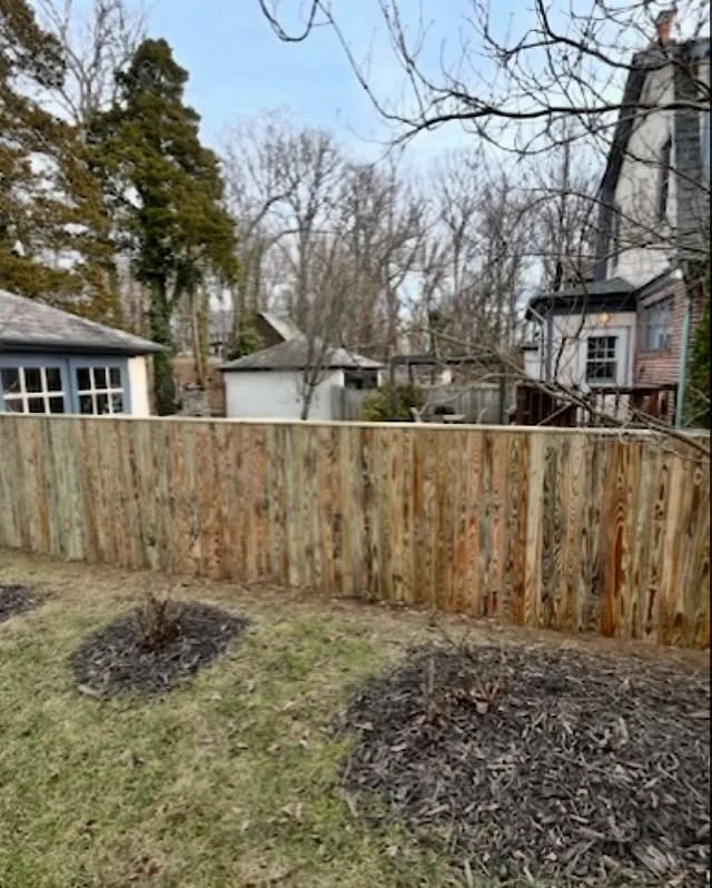 Wooden fence in a backyard with trees and houses in the background