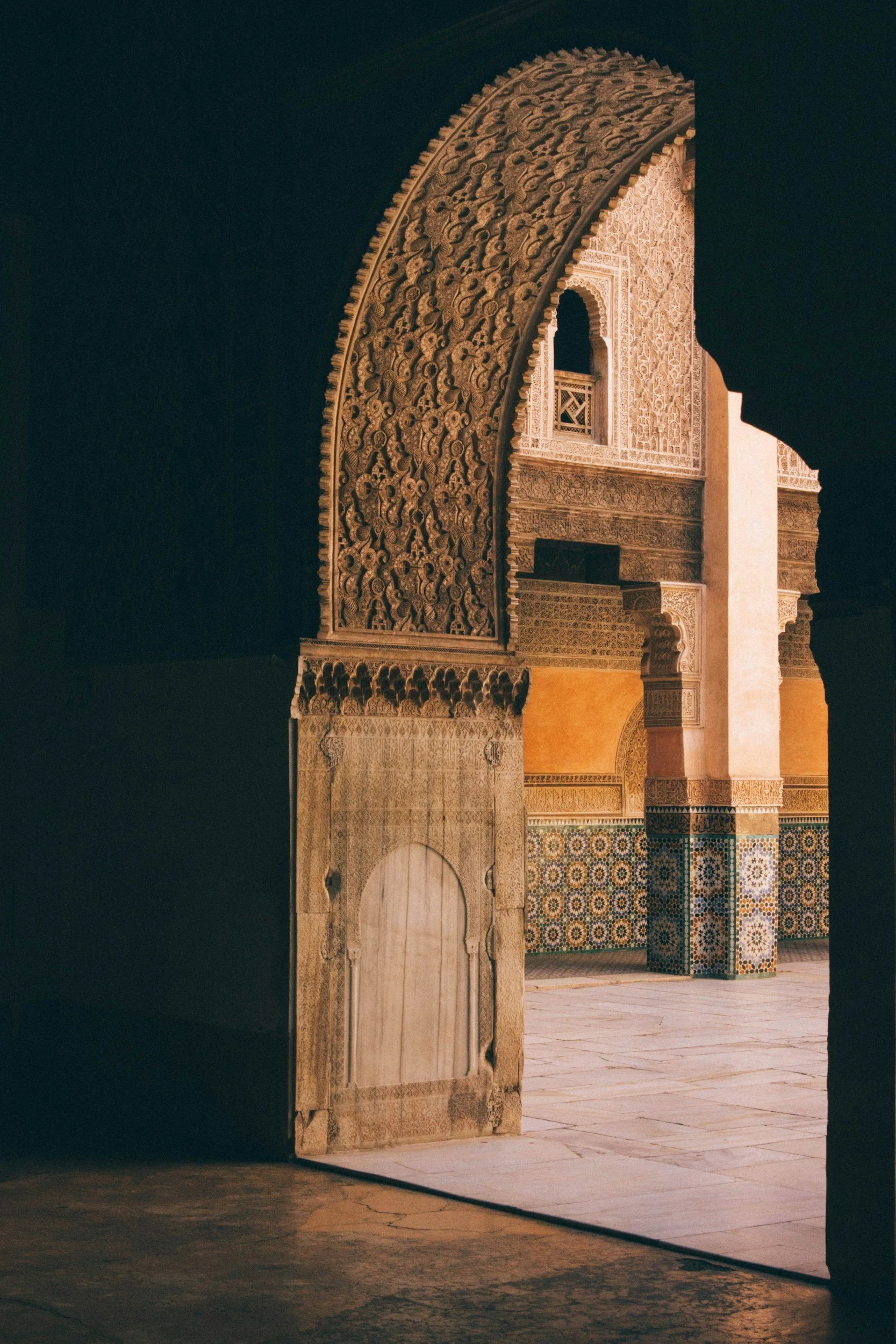 Intricate Moroccan architectural details viewed through a doorway, featuring carved arch and colorful tiled walls.