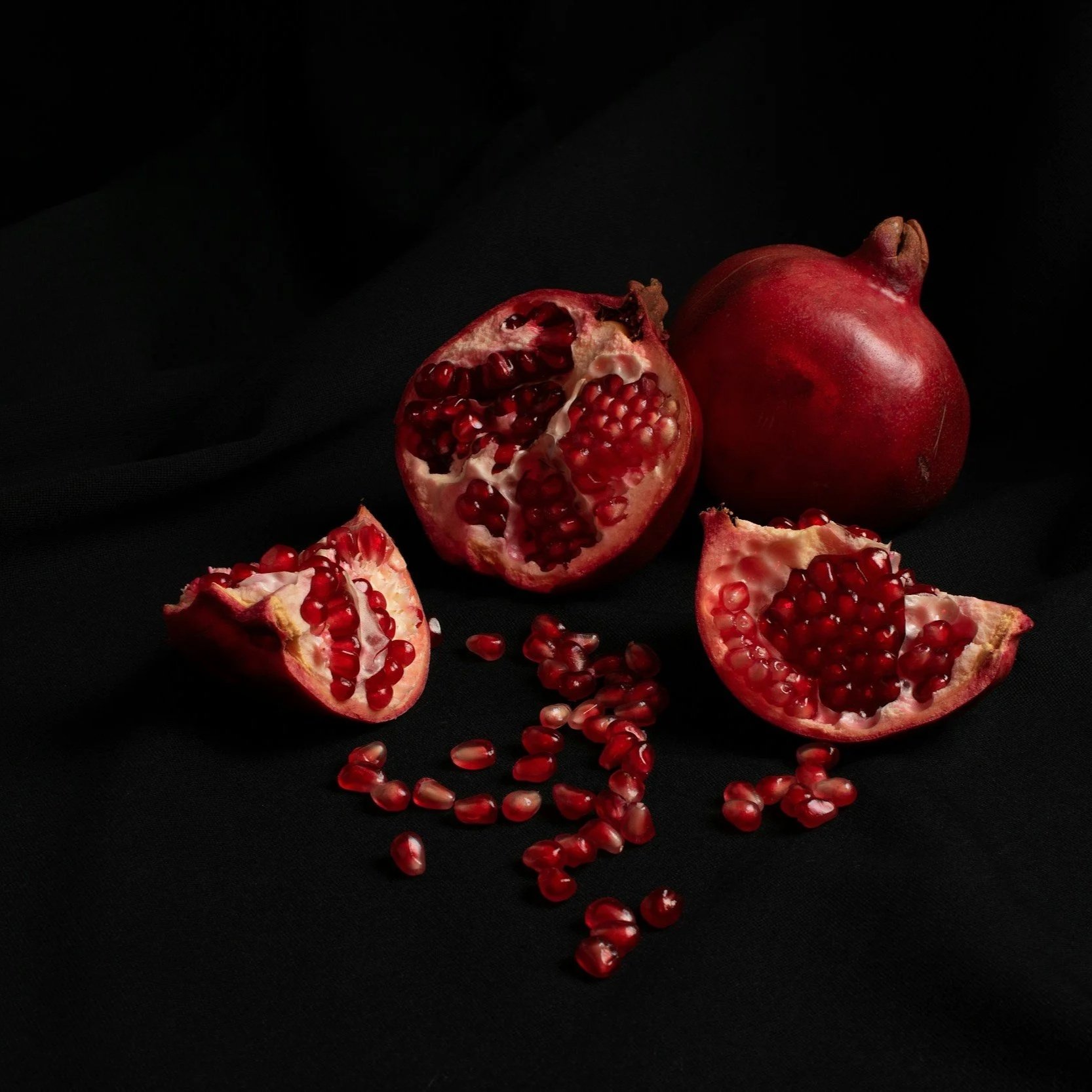 Whole and halved pomegranates on a black cloth background.