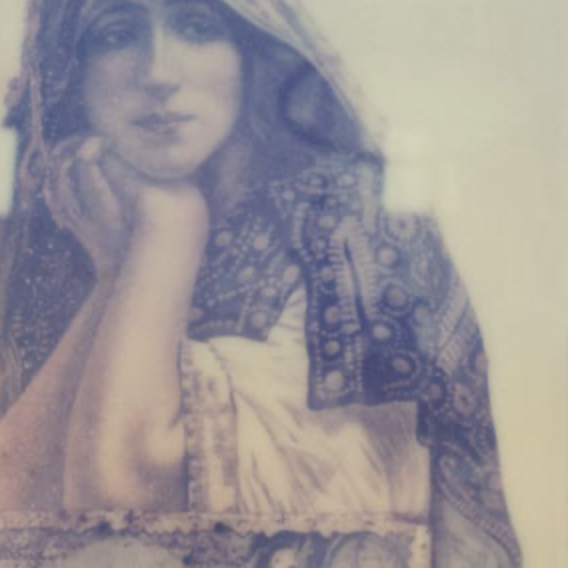 Vintage portrait of a young woman with long wavy hair, wearing a patterned jacket, resting her face on her hand.