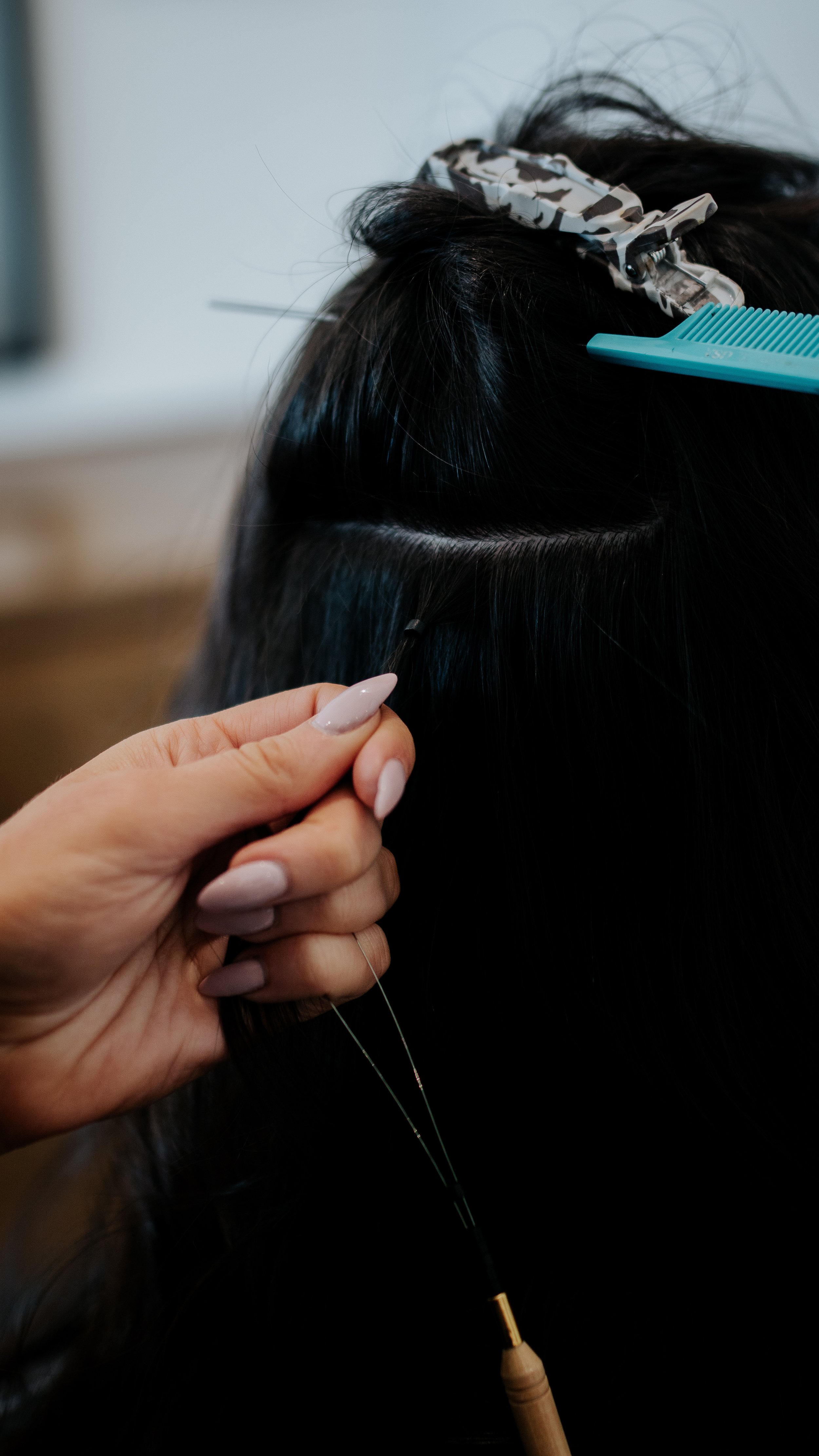 Hair extension application process with a hand holding tools, comb, and hair clip.