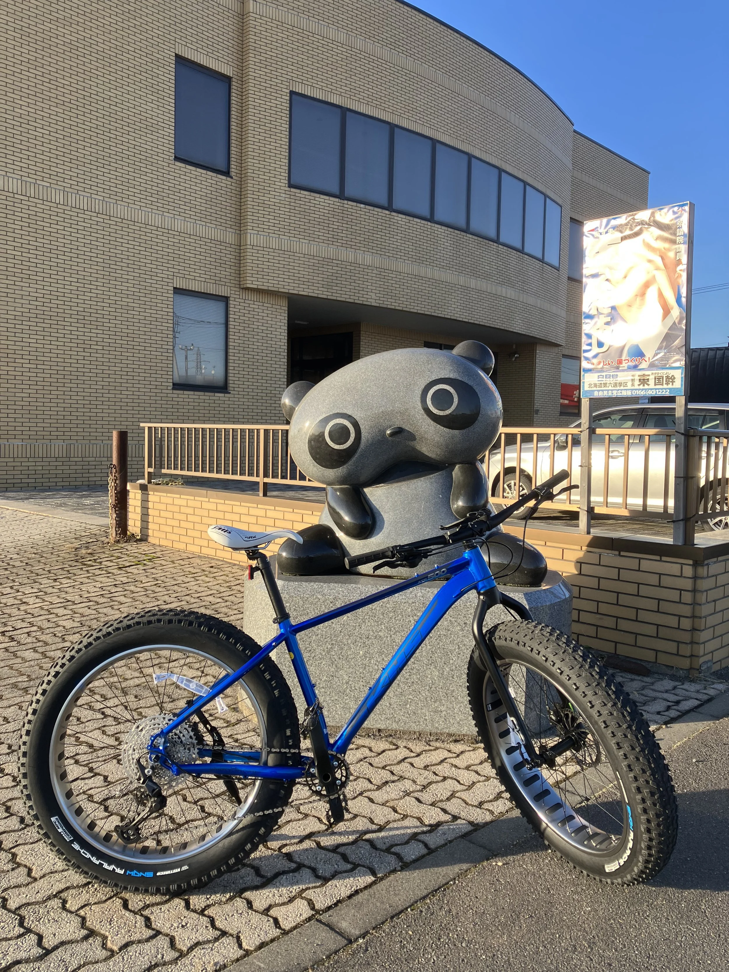 A blue mountain bike parked in front of a panda sculpture on a concrete sidewalk.
