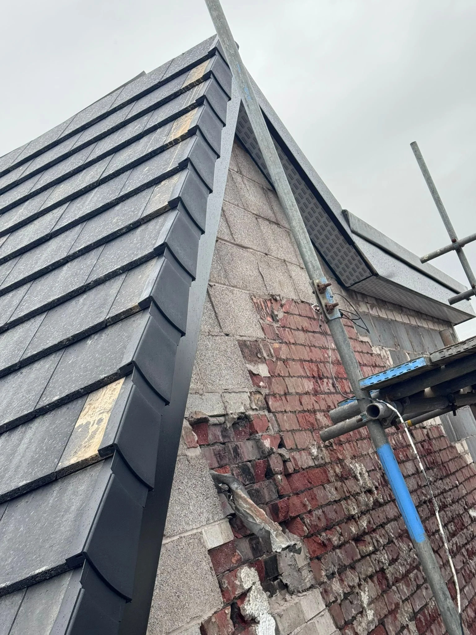 Construction scaffolding next to a brick wall with roofing tiles being installed or replaced on a building.