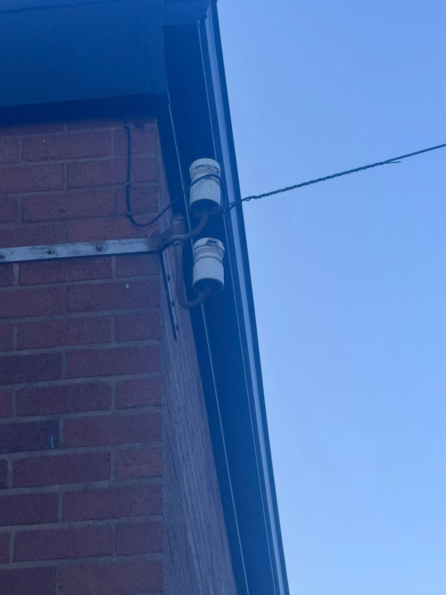 Close-up of a brick building corner with an electrical conduit and a wire against a clear blue sky.
