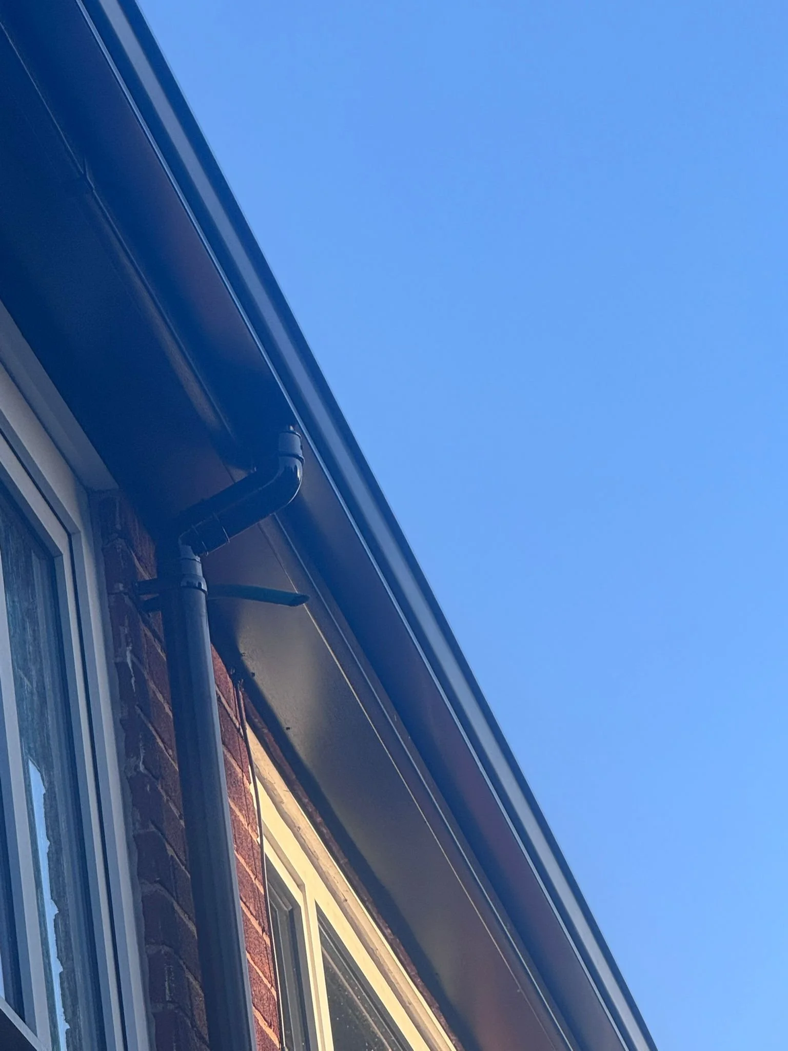 Close-up view of a house exterior showing a section of the window, brick wall, and part of the roof against a clear blue sky.