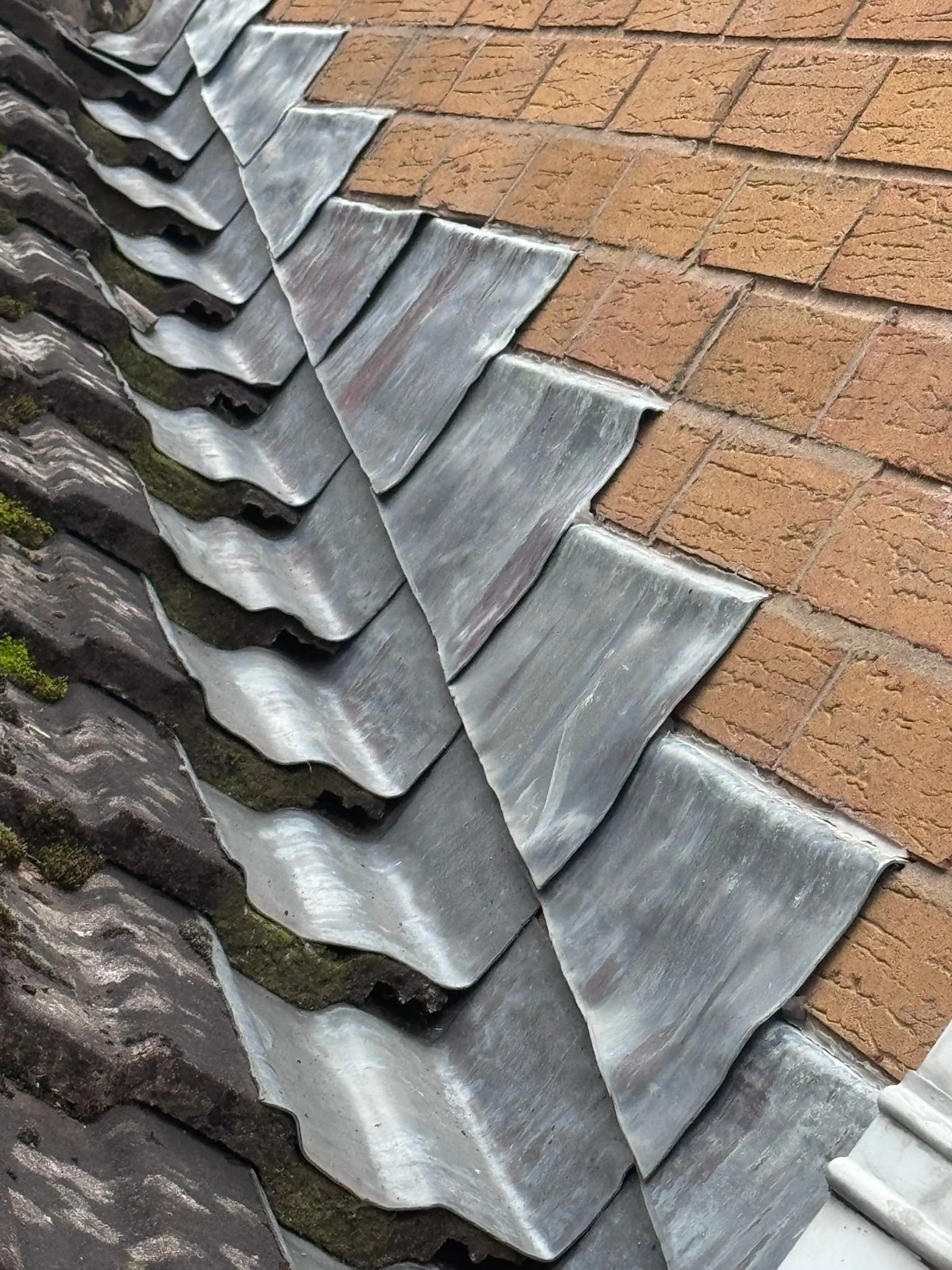 A close-up photo showing the intersection of a brick wall with metal roofing panels, which are weathered and have some moss growth.