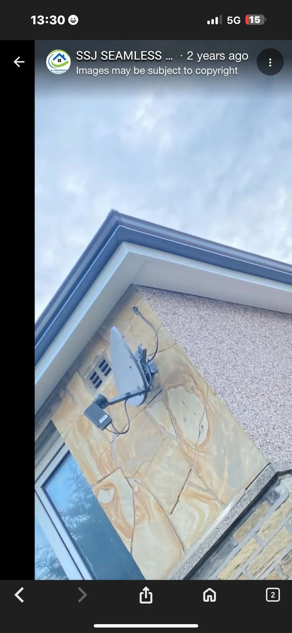 Photo of a section of a house exterior showing a window with a satellite dish installed near it on a marble surface, with a textured wall and a roof at the top.