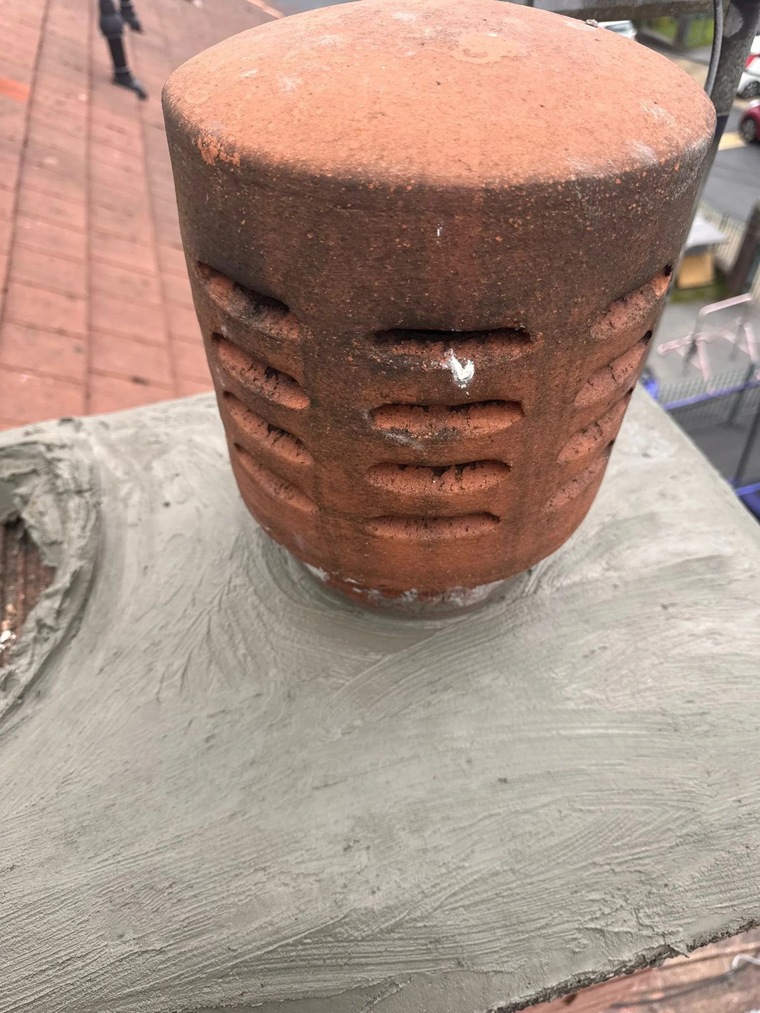 Close-up of a red, rusty, cylindrical ventilation pipe with horizontal slits on a white painted concrete surface.