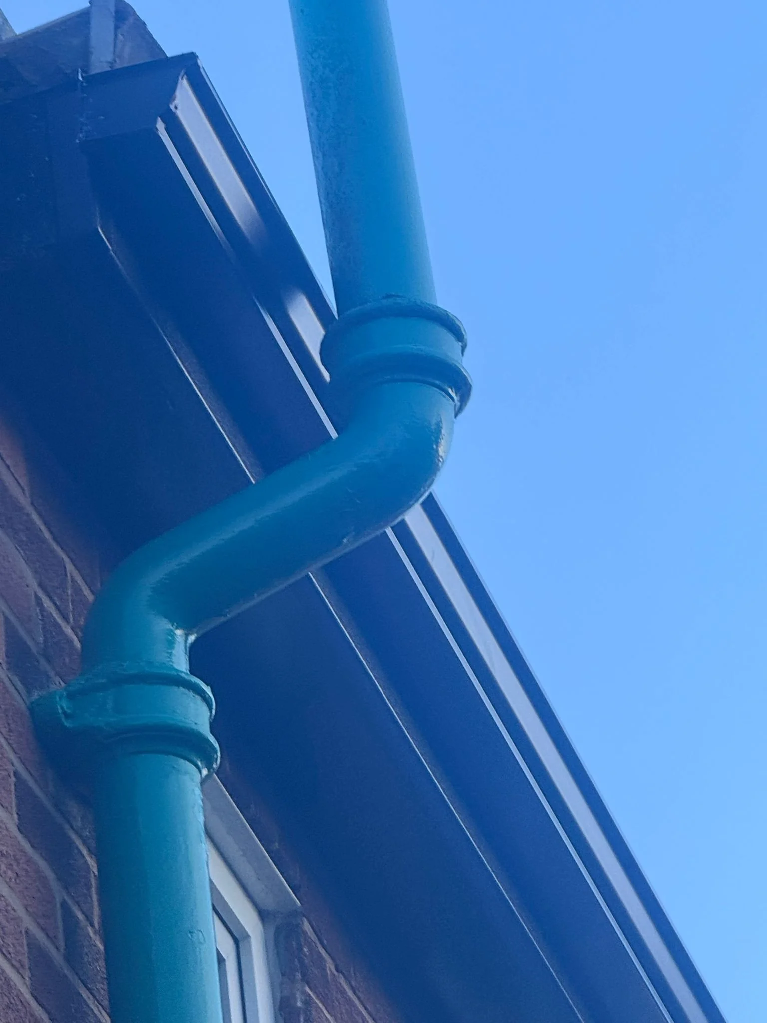 Blue downspout and pipe against a house exterior with a clear blue sky.