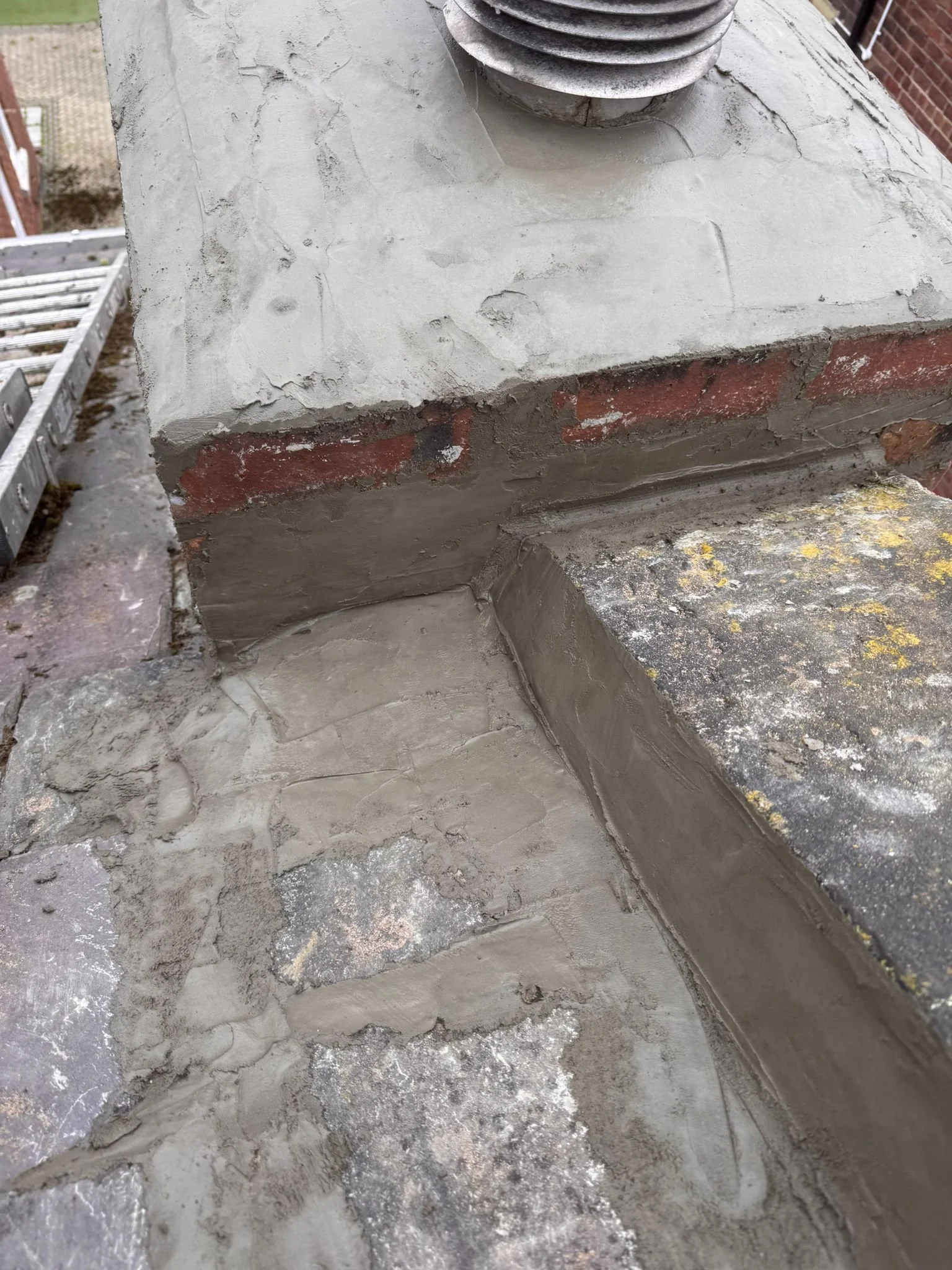Close-up of a concrete rooftop corner with ductwork, brick, a metal ladder, and construction debris.