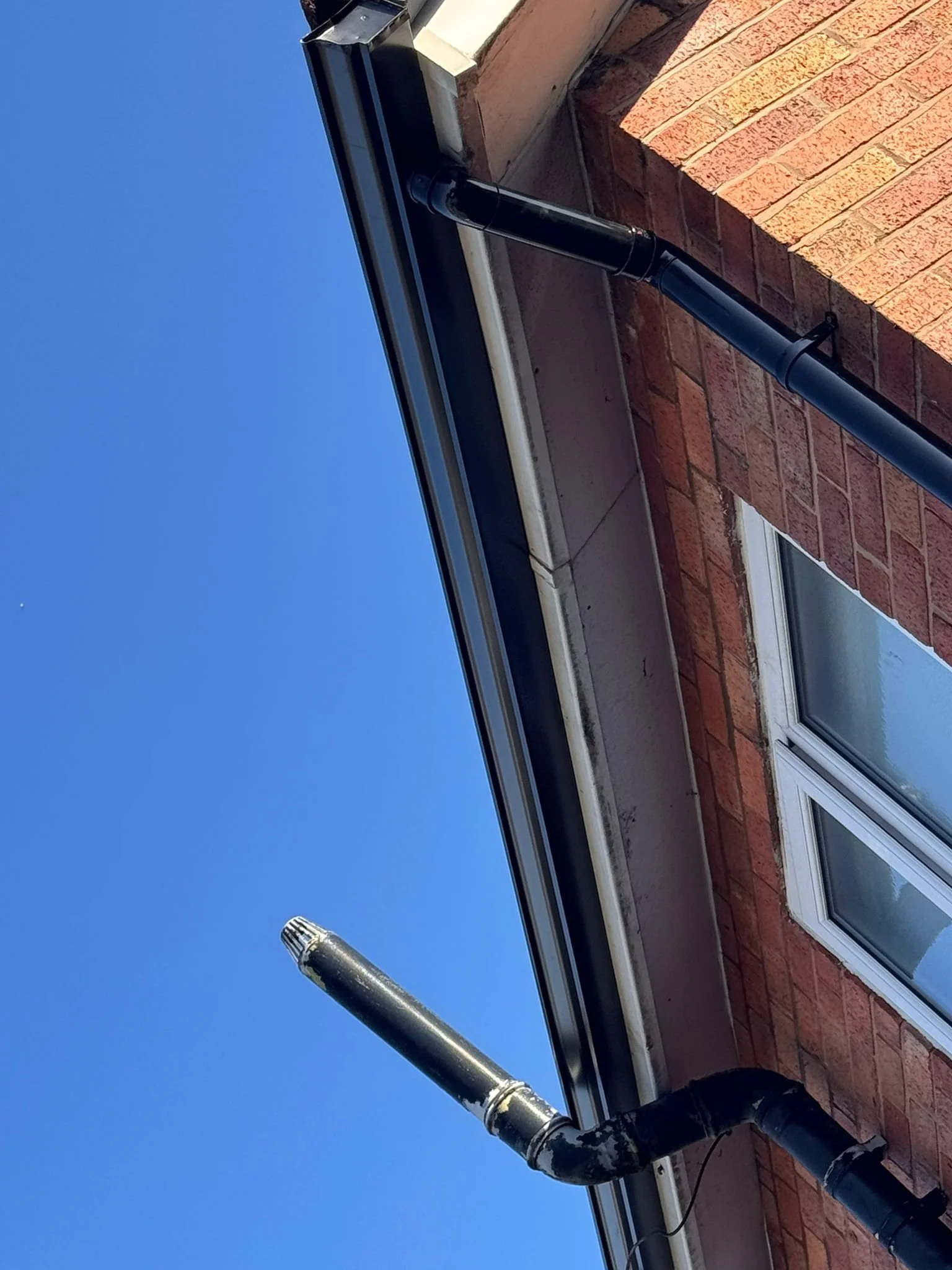 A black metal vent pipe extending from the side of a building with a brick exterior, under a clear blue sky.