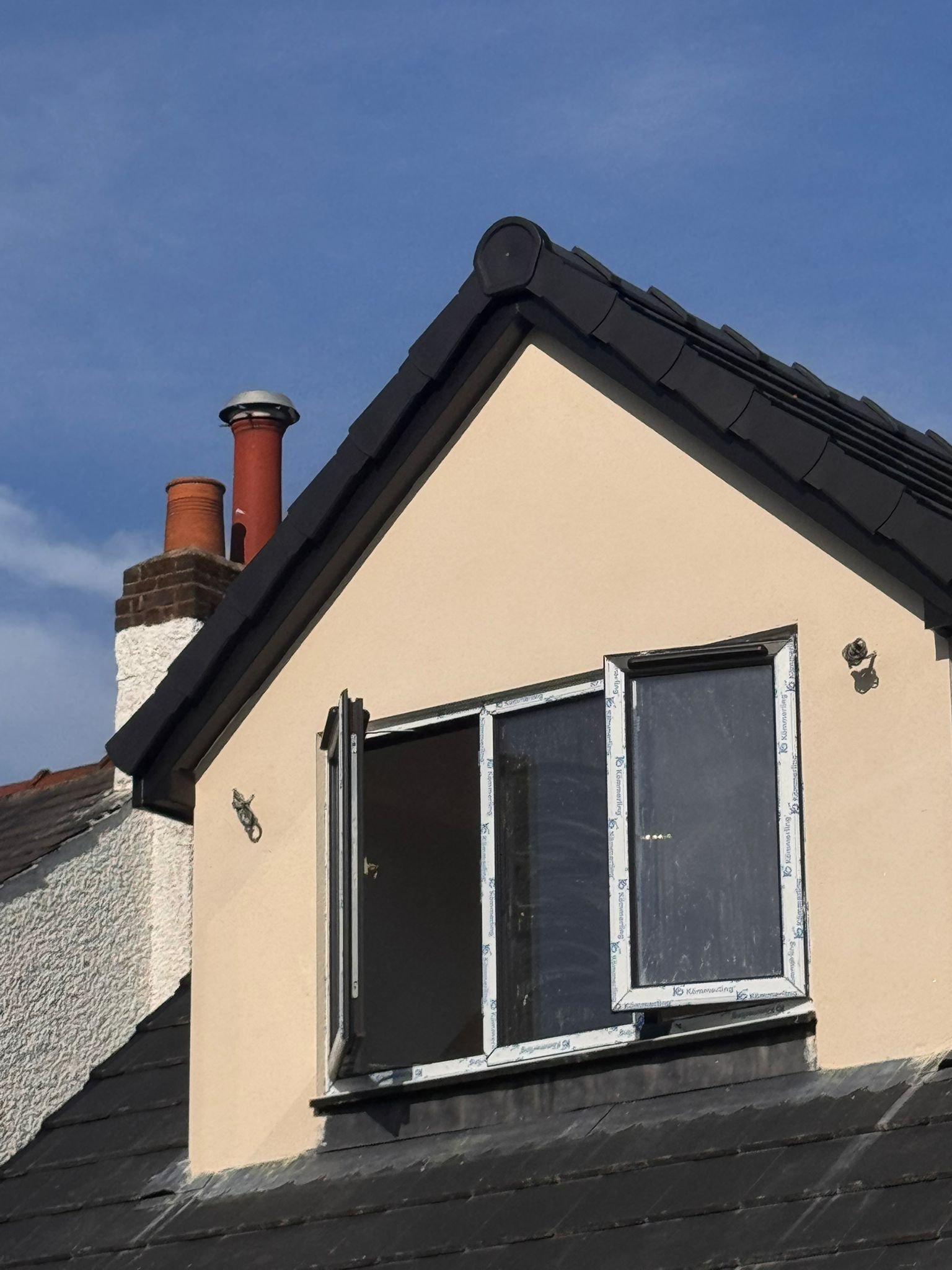 A house rooftop with three chimney stacks and an opened skylight window.