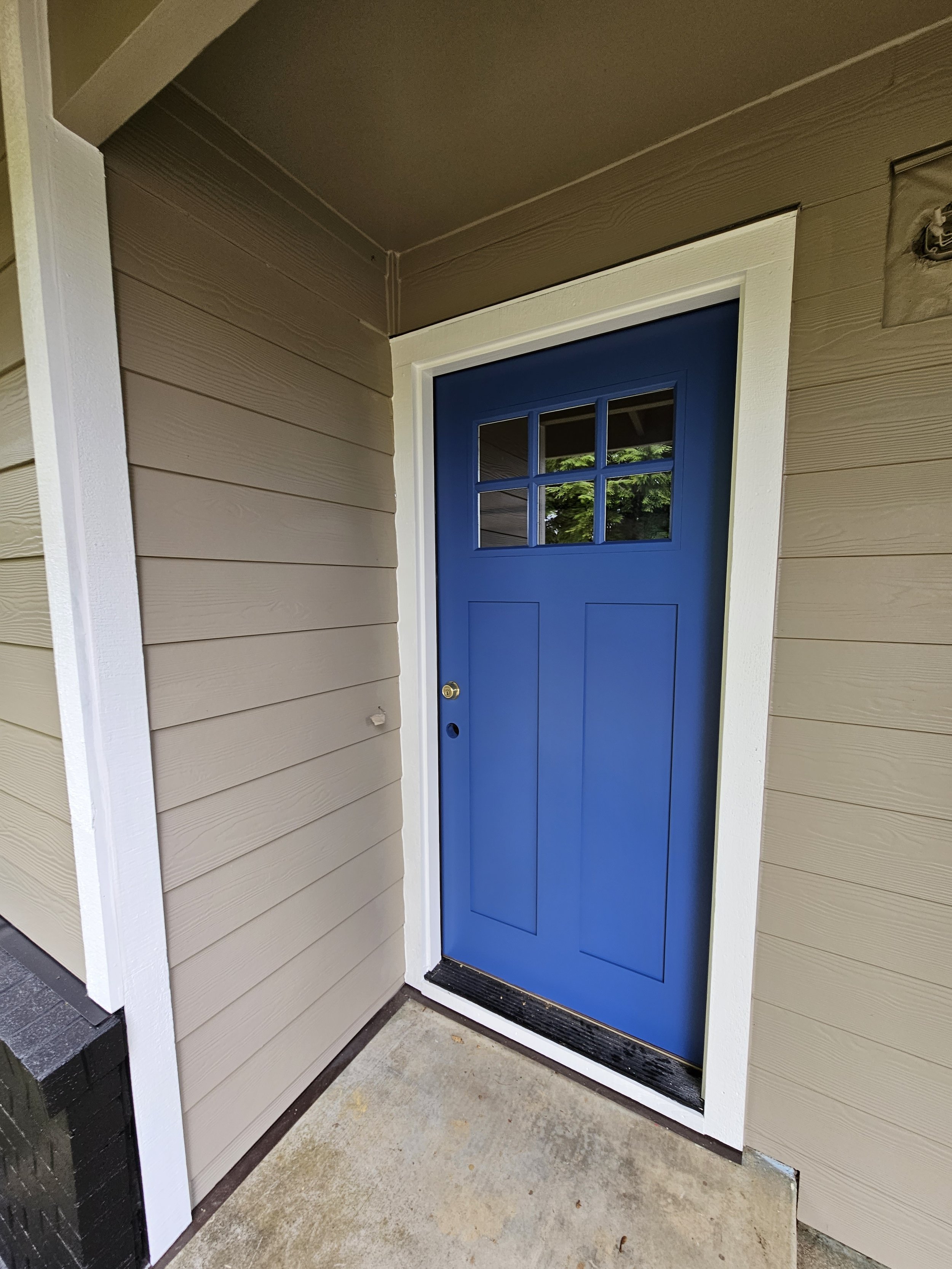 Blue front door with six small window panes, beige siding, and white trim.