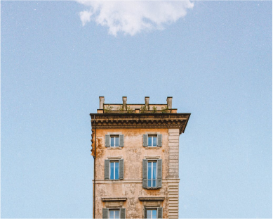 Close-up of a tall, old brick building with a flat roof, set against a clear blue sky with a few clouds.