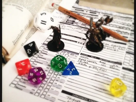 Tabletop with role-playing game components, including painted miniatures, various dice, a pencil, and a character sheet.